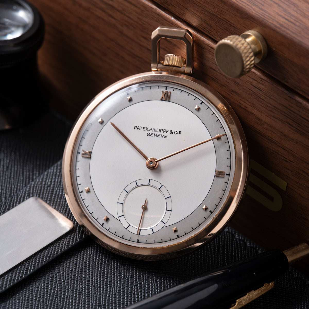 Rose gold pocket watch with white dial, Roman numerals, center hands, and subsidiary seconds dial on wooden surface.
