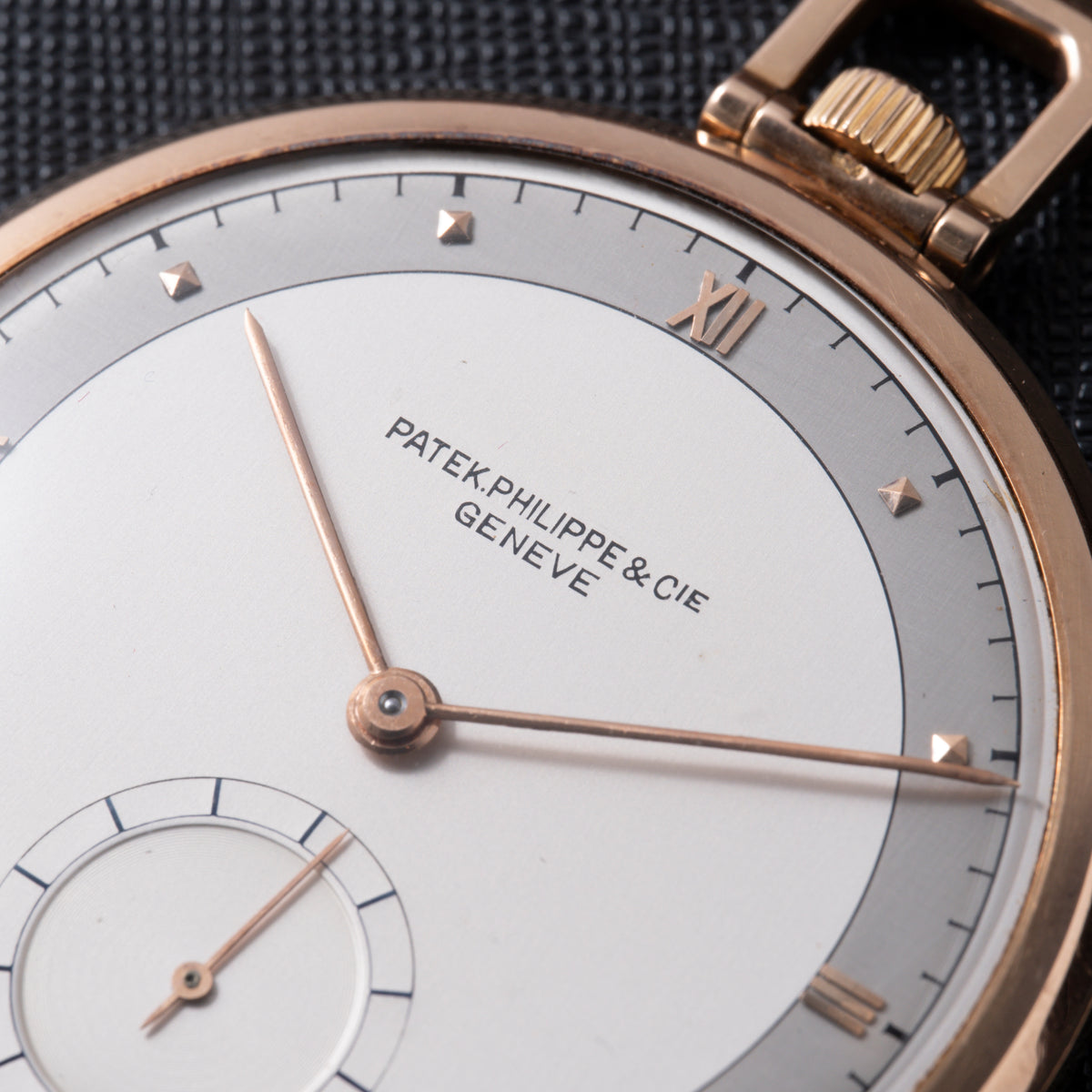 Rose gold pocket watch with white dial, Roman numeral markers, subsidiary seconds dial, and crown visible at top right.
