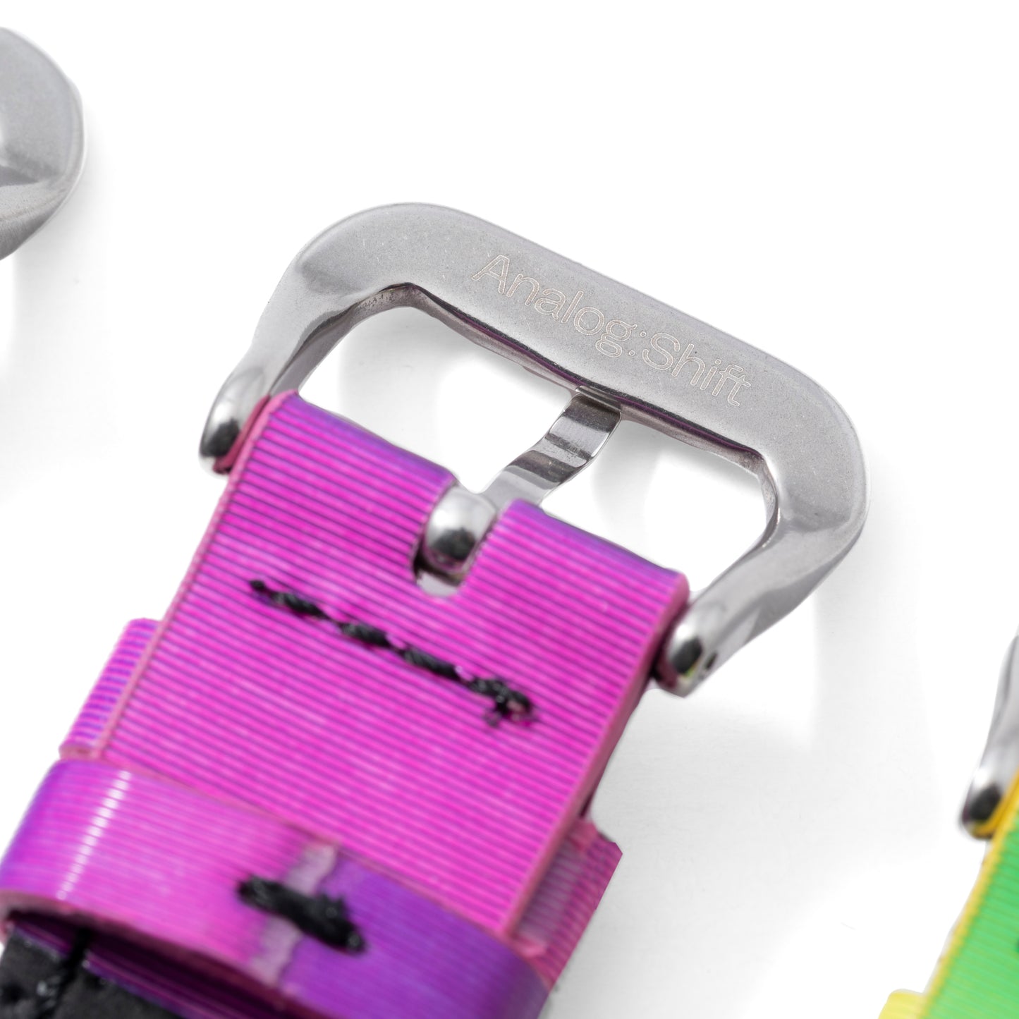 Close-up of a metallic watch buckle engraved with Analog:Shift, attached to a vibrant pink and purple Grabber Orange Effect Matrix Strap with black stitching, set against a white background.