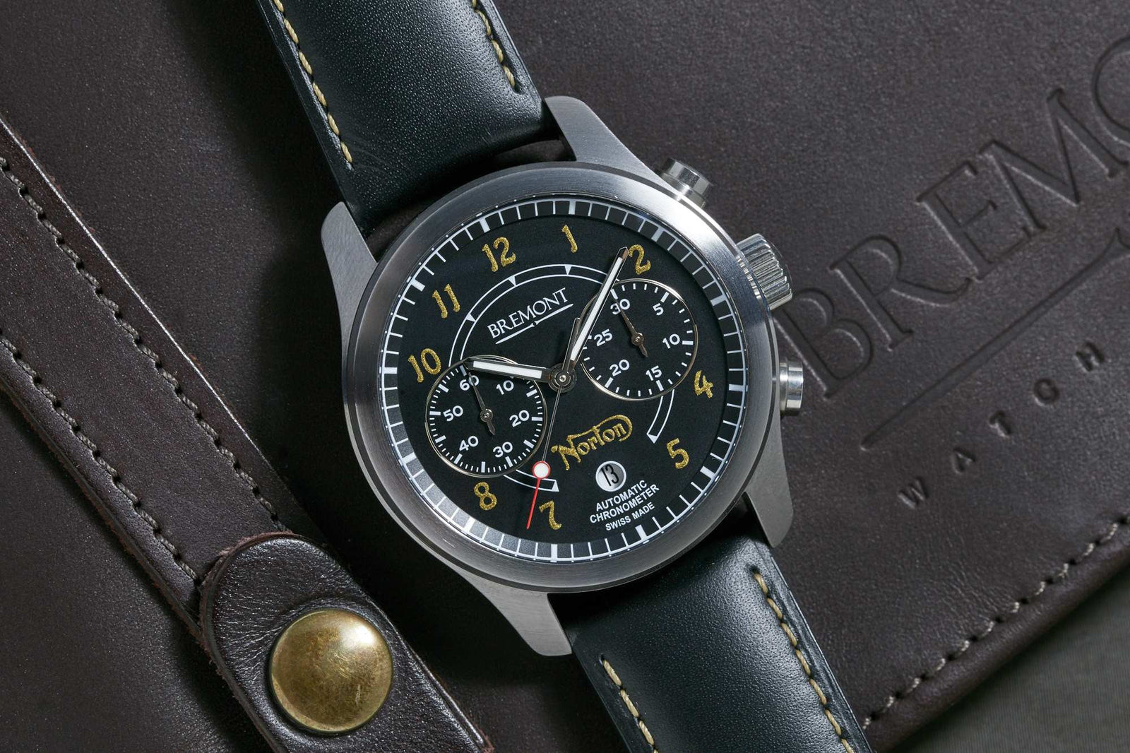 The Bremont Norton Limited Edition Chronograph, featuring a black dial with yellow numerals, chronograph subdials, and a black leather strap, is displayed on a brown leather Bremont case embossed with the brand’s logo.