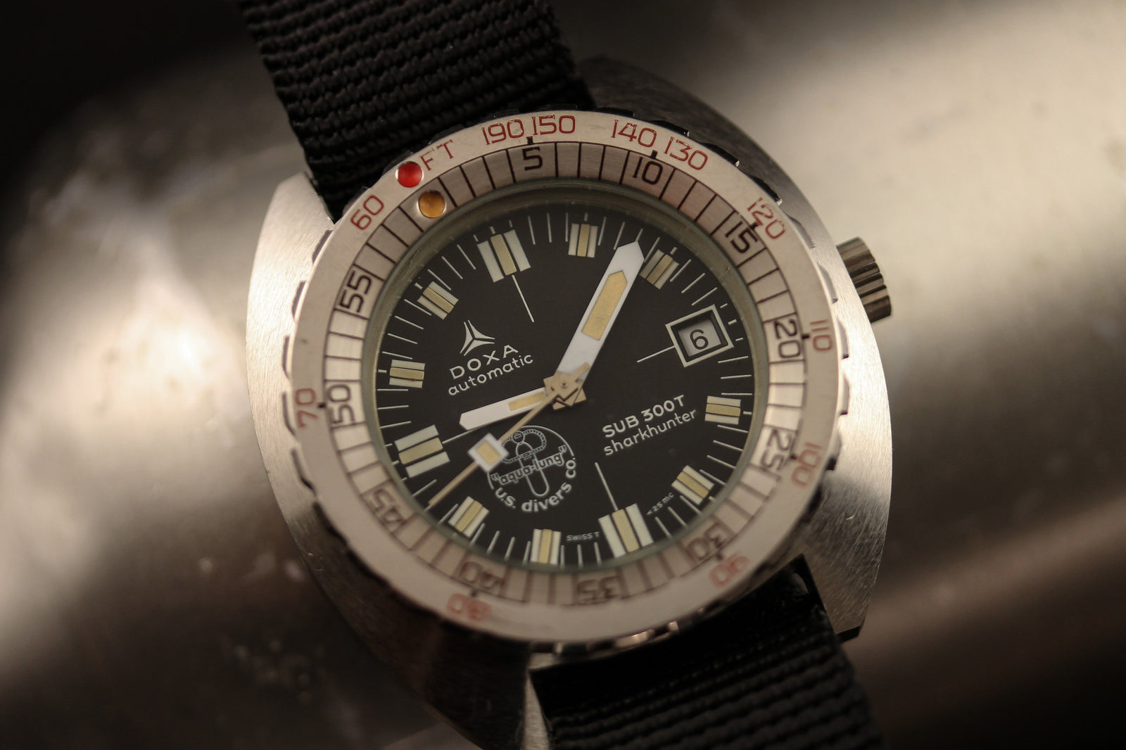 Close-up of the DOXA Sub 300T Sharkhunter Aqua Lung, an automatic dive watch with a black dial, silver bezel, black fabric strap, date display, luminous hands and markers, "SUB 300T professional" text, and the Aqua Lung logo.