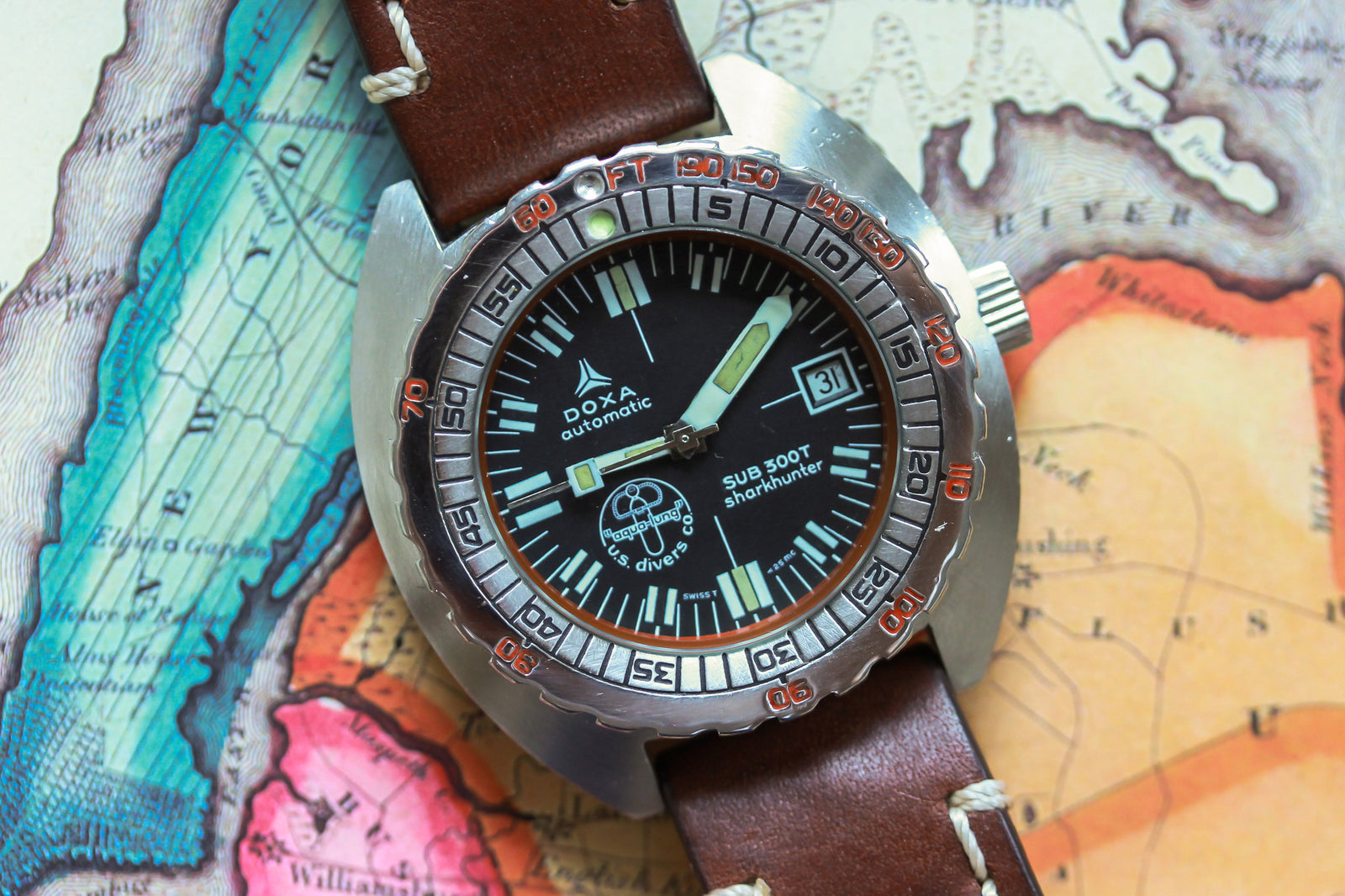 A DOXA Sub 300T Sharkhunter Aqua Lung automatic dive watch, celebrated by legendary divers, rests on a vintage map—its black dial, bold hour markers, and orange-accented rotating bezel stand out prominently.