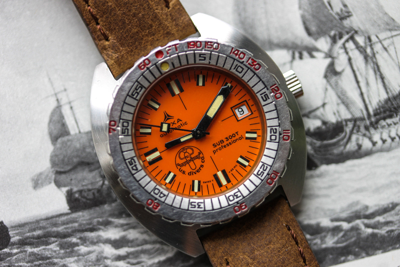A close-up of the DOXA Sub 300T Professional Aqua Lung shows an orange dial, brown leather strap, silver bezel, and black, white, and red details against a grayscale sailing ship background.