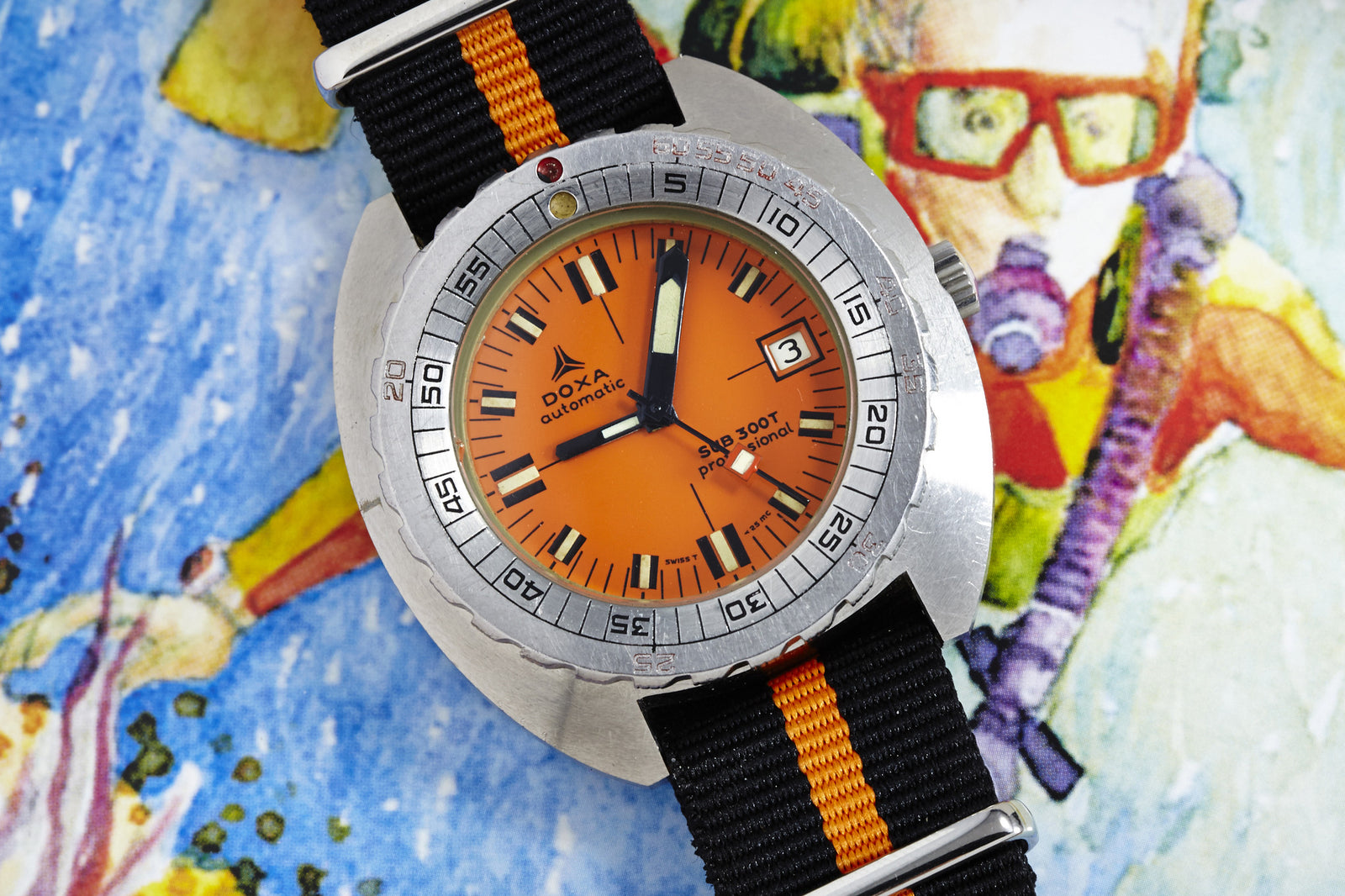 A DOXA Sub 300T Professional - Synchron Dial dive watch with an orange face and black-orange NATO strap sits on a vibrant diver illustration, showing the date as the 3rd.