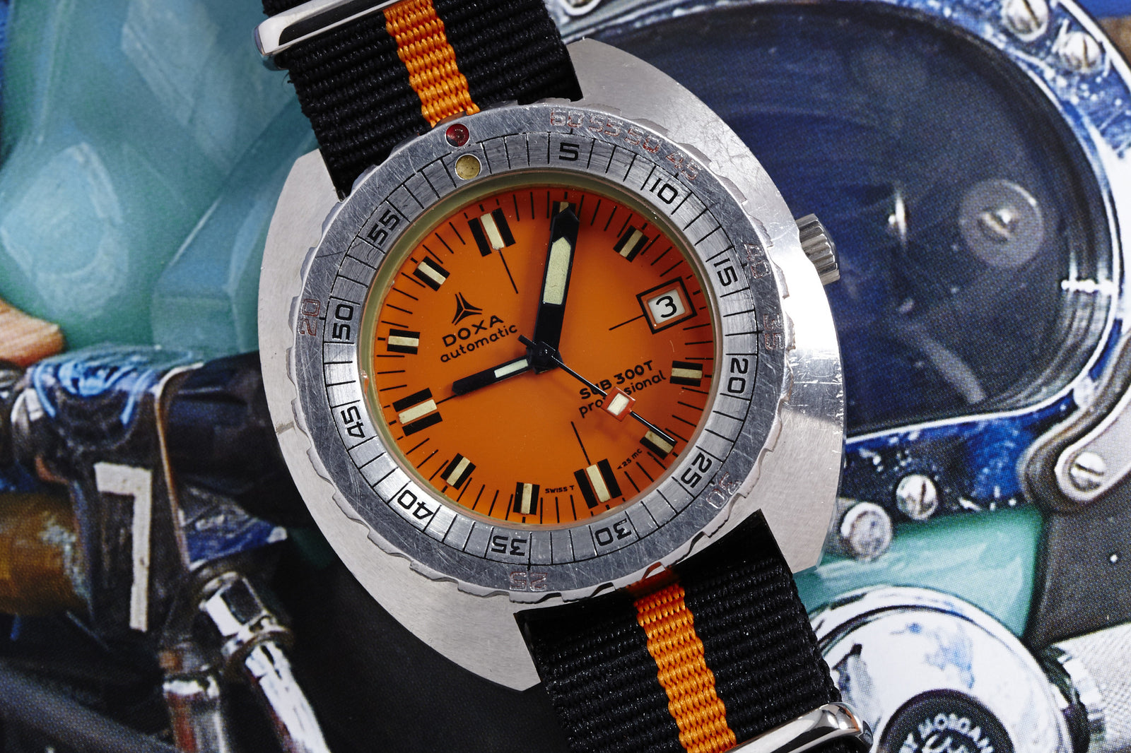 A close-up of the DOXA Sub 300T Professional - Synchron Dial watch with an orange face and black-orange striped nylon strap, set to the 3rd, on a vibrant, motorcycle-themed background.