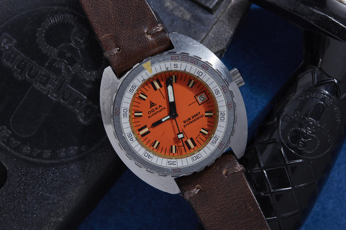 Stainless steel diving watch with bright orange dial, brown leather strap, and rotating bezel with minute markings.