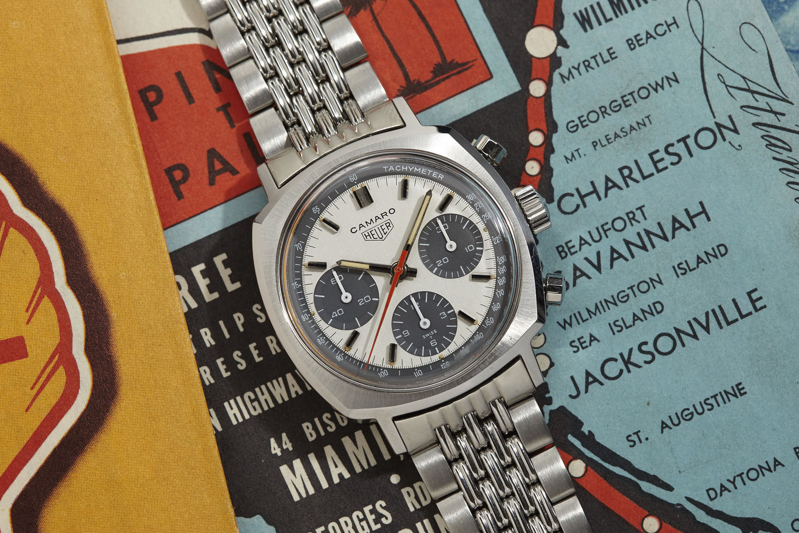 A Heuer Camaro Exotic Dial watch with striking panda dials rests on colorful vintage travel maps featuring destinations in the southeastern United States, such as Miami and Savannah.