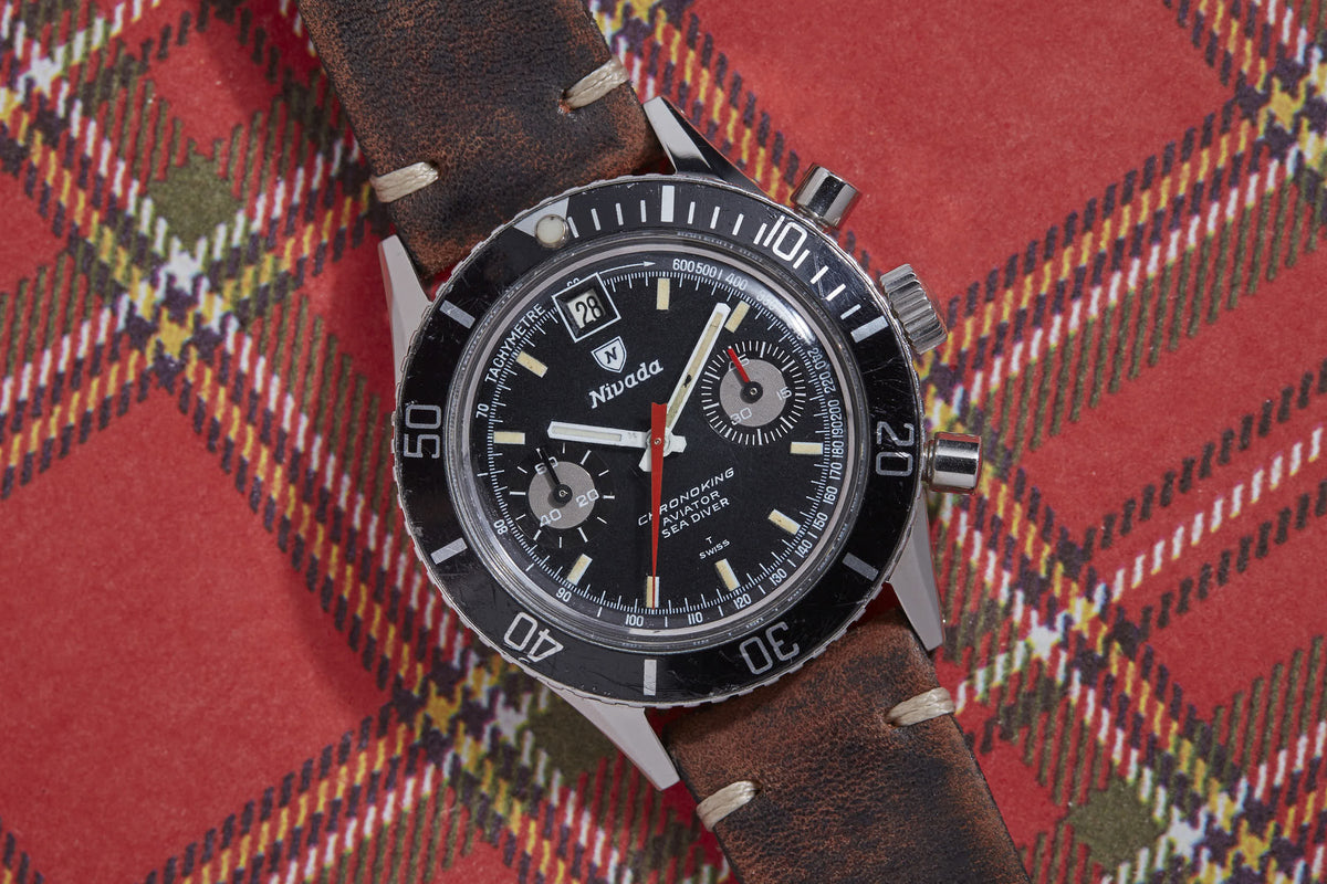 Nivada Chronoking Date watch with black dial, chronograph subdials, date window, and brown leather strap on plaid background.