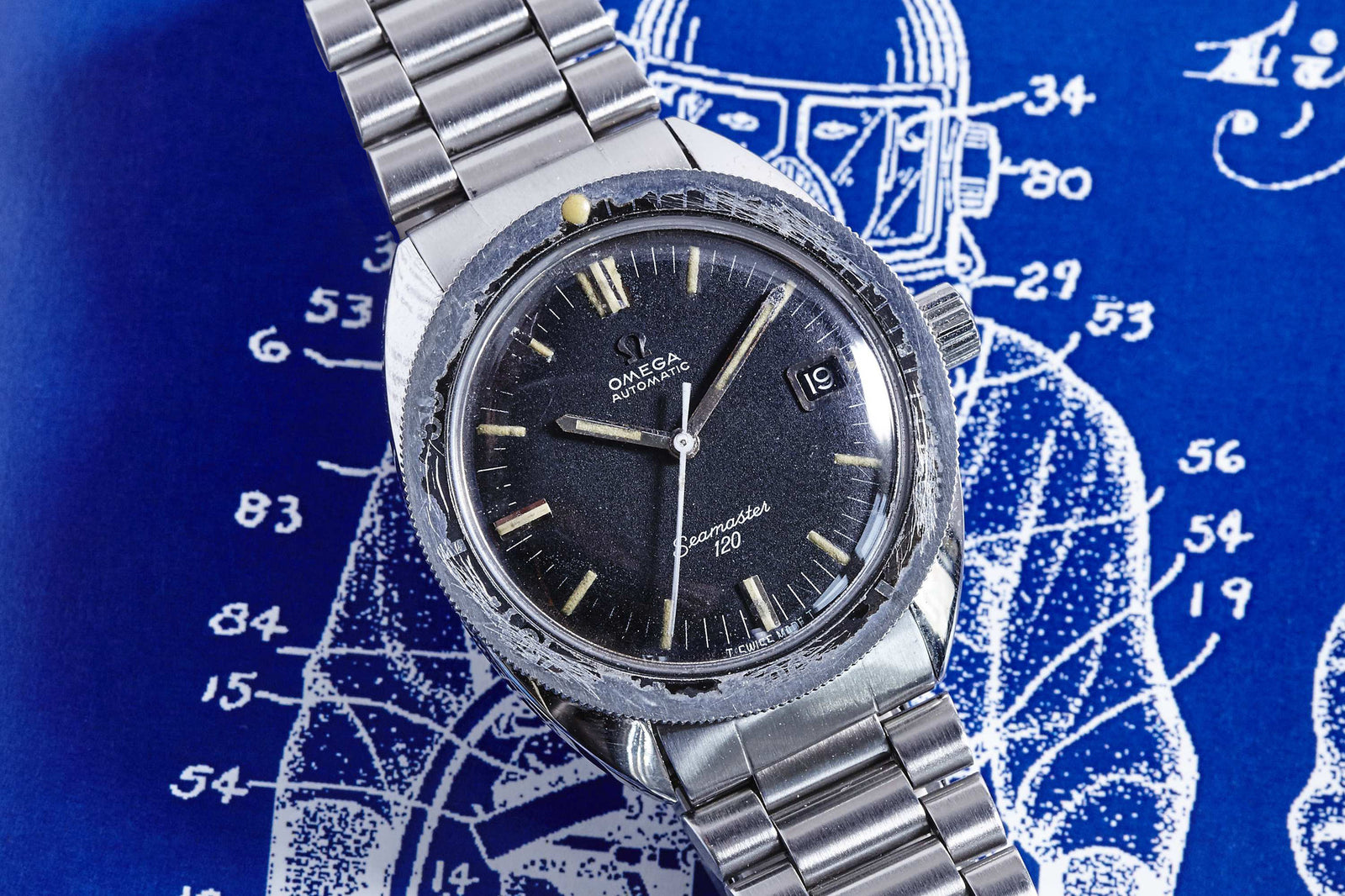 An Omega Seamaster 120 vintage sports watch by Omega with a stainless steel band, displayed on a blue background featuring a white schematic drawing and numbered labels.