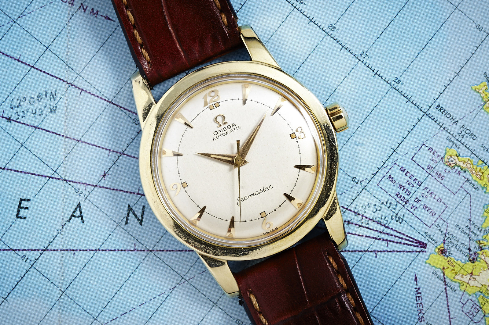 The Omega Seamaster Automatic - Yellow Gold Filled by Omega, featuring a brown leather strap and Calibre 354 movement, sits on a blue map of the Pacific, its vintage dial showing 2:45.