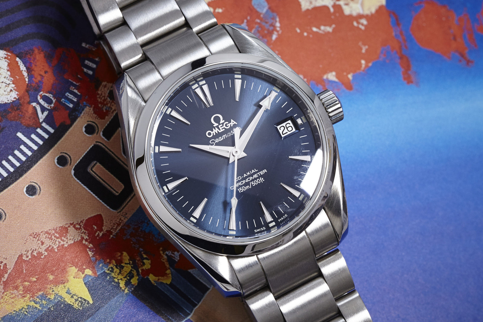 An Omega Seamaster Co-Axial Ref. 2504 with a 36mm stainless steel case, dark blue dial, date display, and metal bracelet shows 10:10 on a vibrant abstract map. Comes with original box and papers. Brand: Omega.