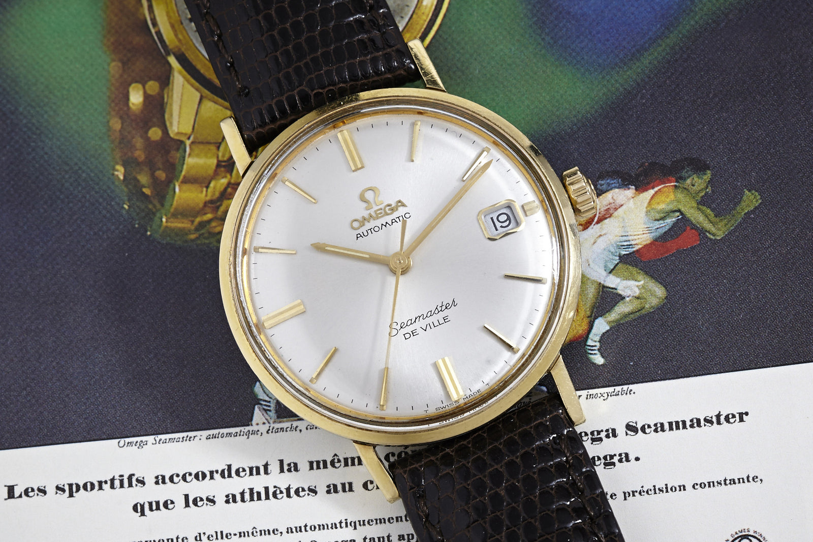 An Omega Seamaster De Ville Automatic wristwatch with a white dial and black leather strap is displayed atop a vintage ad showing a running athlete in the background.