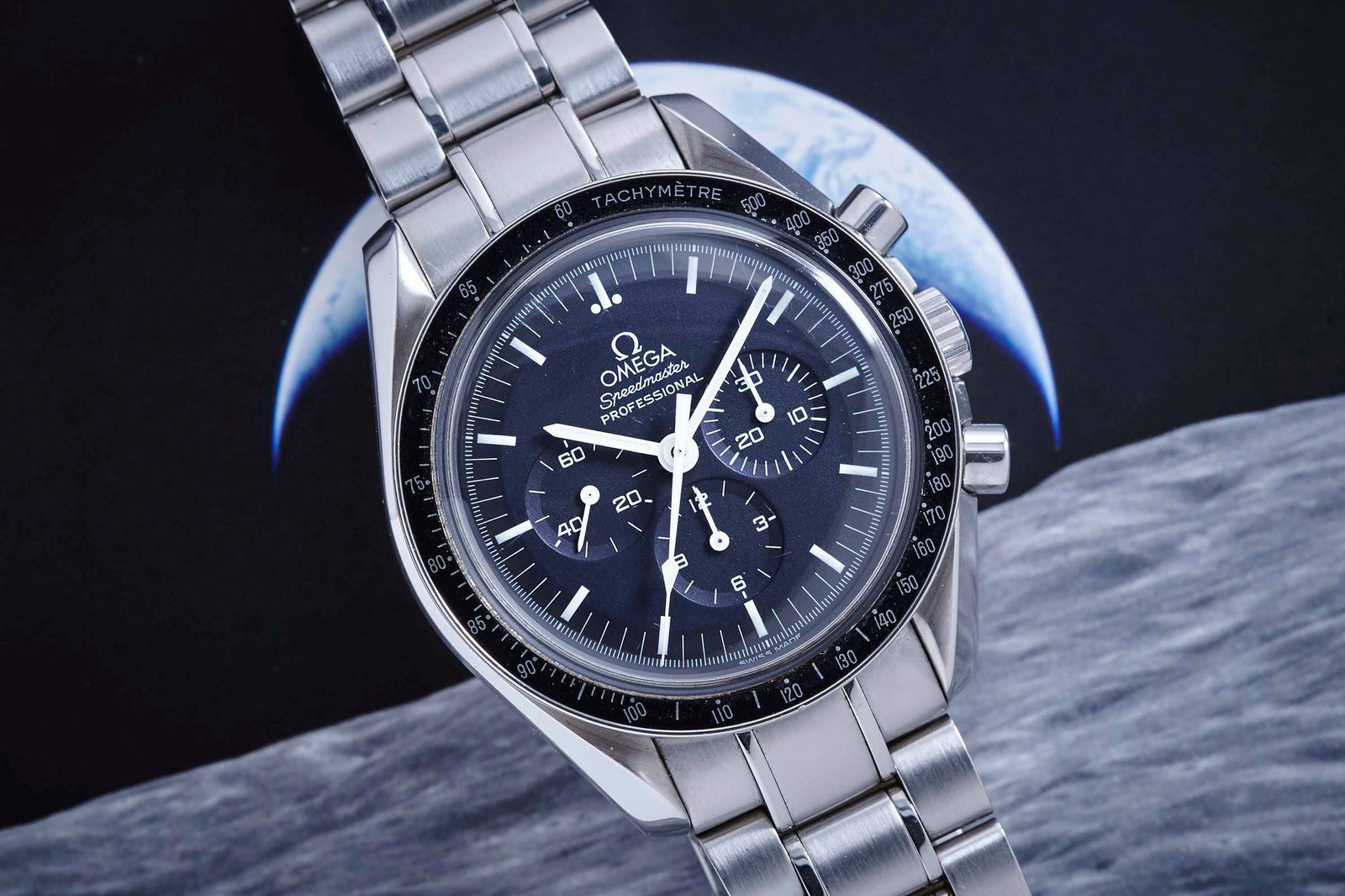 A close-up of the Omega Speedmaster by Omega, featuring a stainless steel band, set against the Moon with Earth rising—evoking the Apollo era’s adventurous spirit.