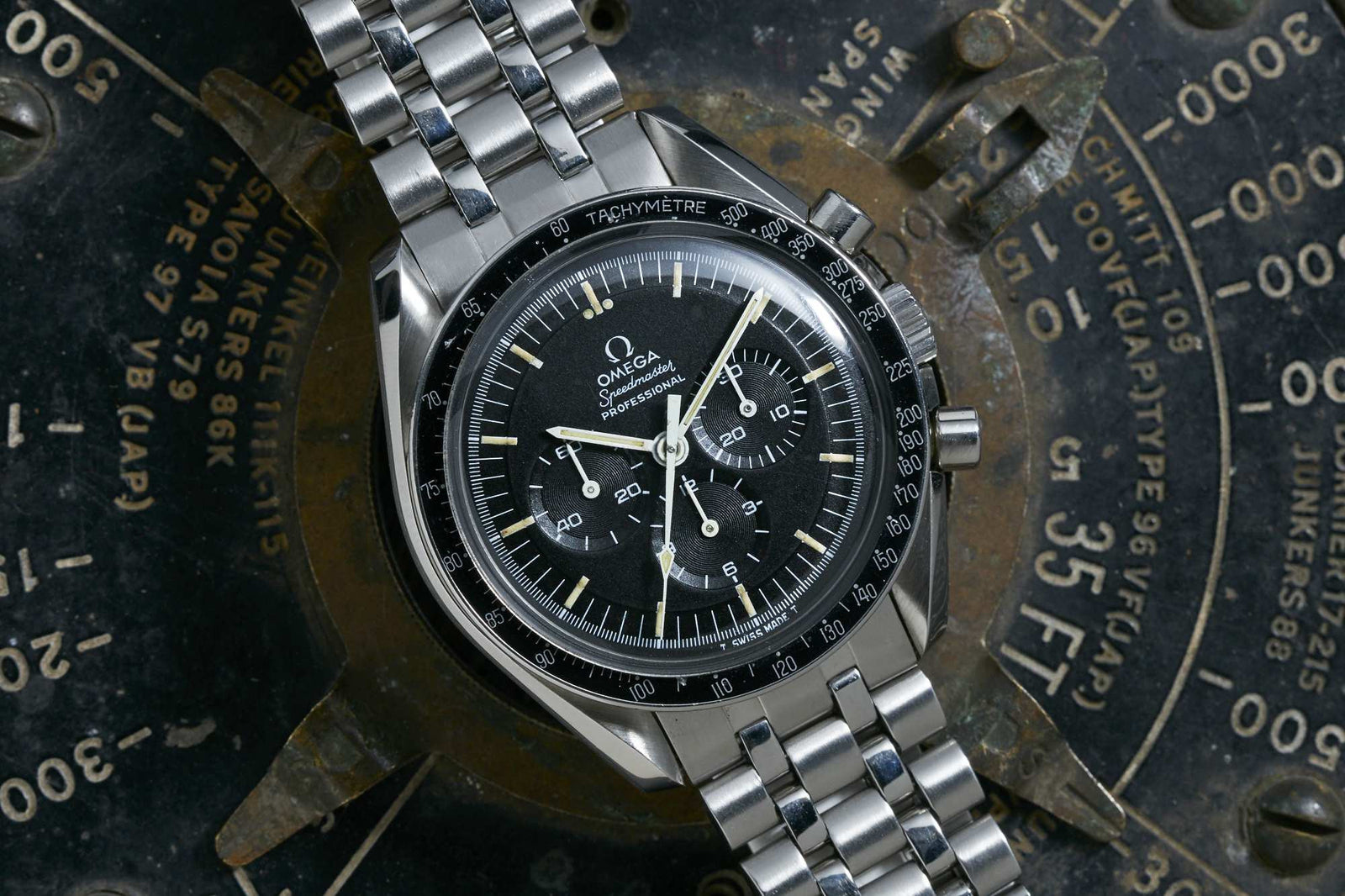 A close-up of an Omega Speedmaster Professional by Omega, featuring a black dial and stainless steel bracelet, displayed on an aged instrument panel. Detailed description coming soon!.