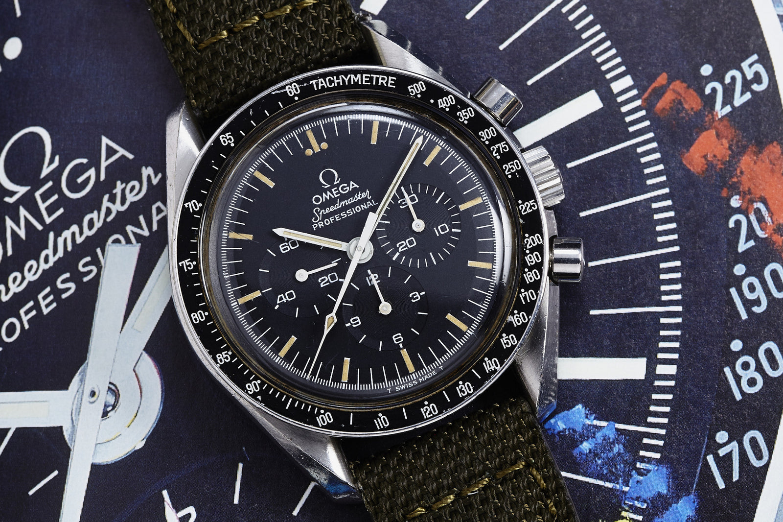 A close-up of the Omega Speedmaster Professional - 1983 by Omega, featuring a black dial and tachymeter bezel, resting on a colorful background with an enlarged watch face design.