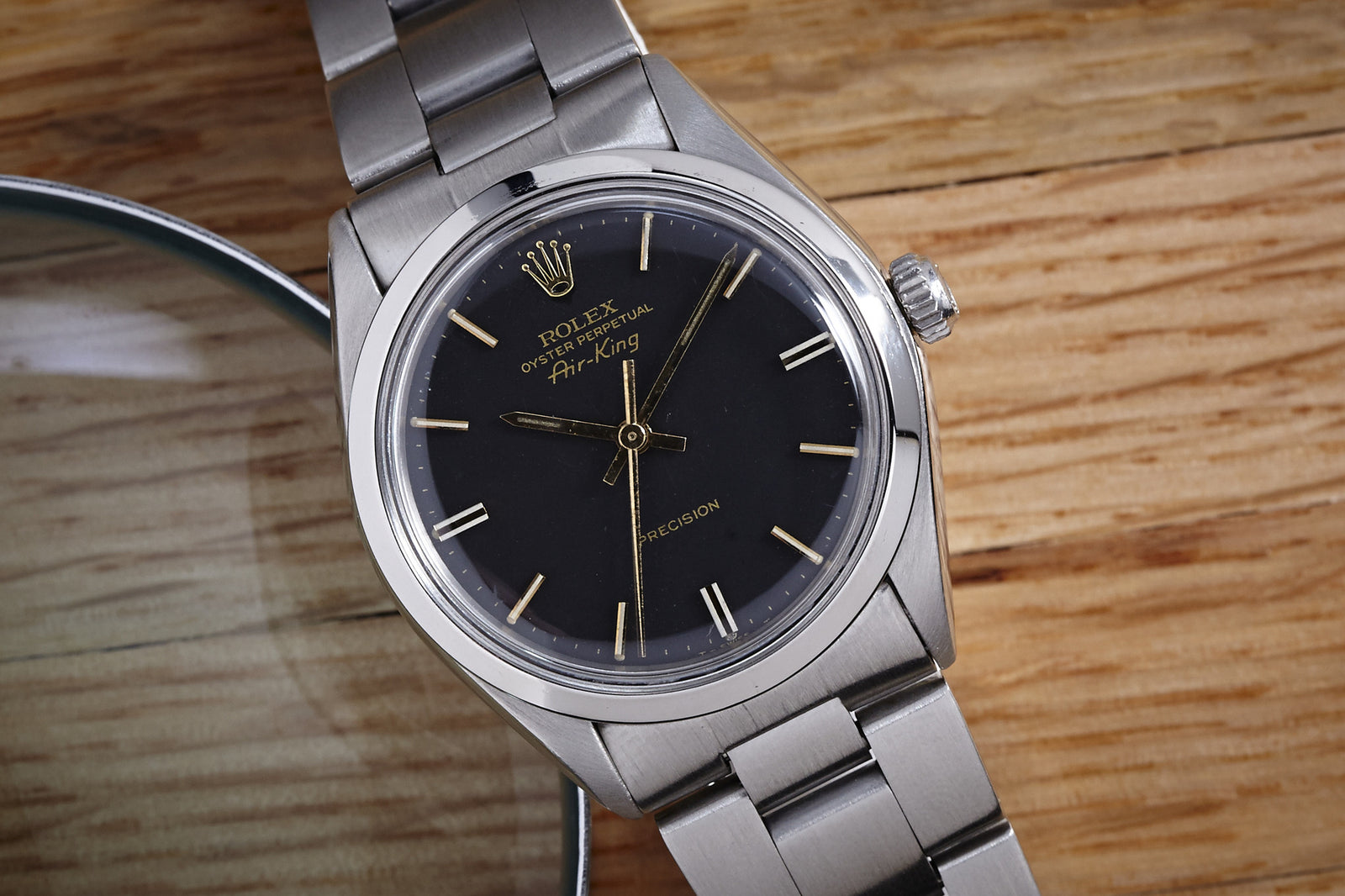 A 1977 Rolex Air King Gilt Dial rests on a wooden surface beside a magnifying glass, highlighting the brand’s iconic Oyster Case and timeless elegance.