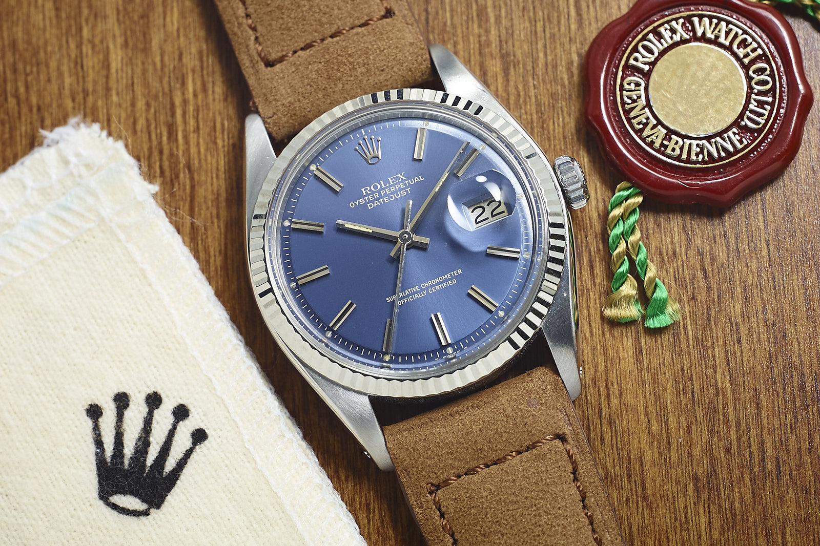 A Rolex Datejust 1601 Blue Dial - 1977 rests on wood beside a Rolex cloth with the crown logo and a red wax seal featuring green and gold string.