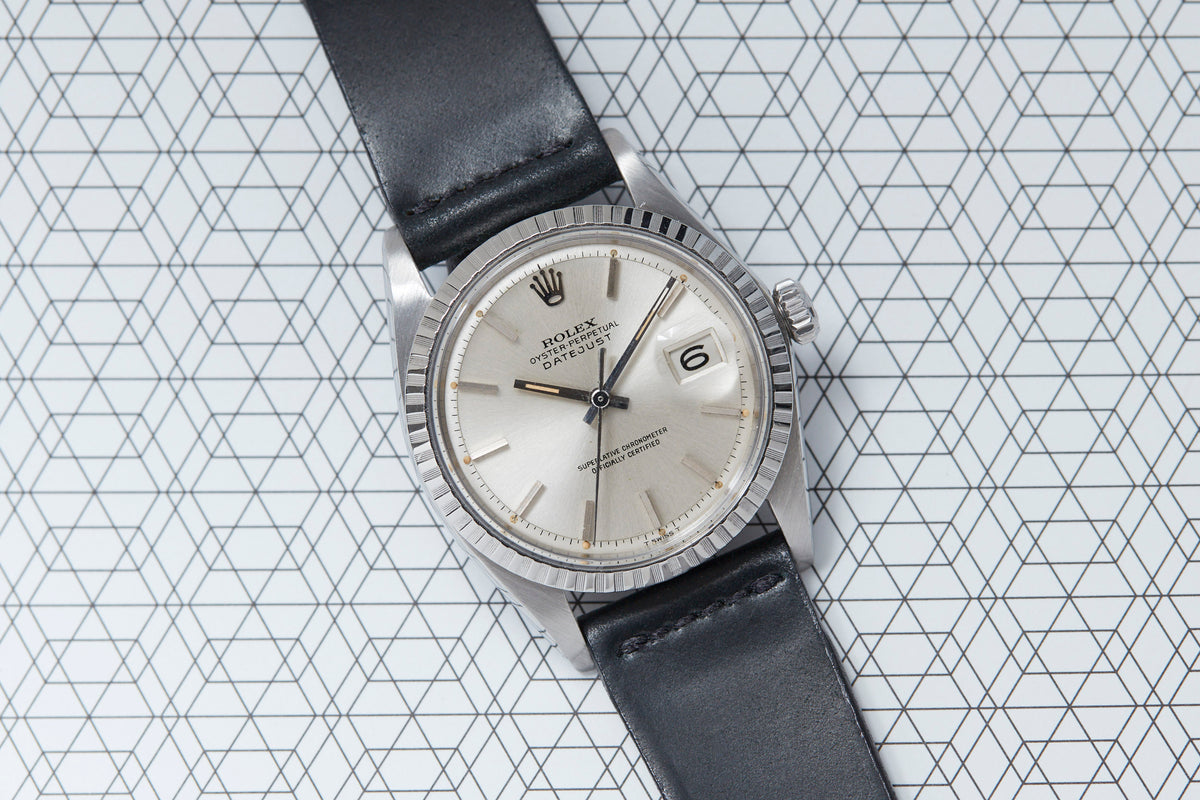 Stainless steel watch with silver dial, date window at 3 o'clock, fluted bezel, and black leather strap.