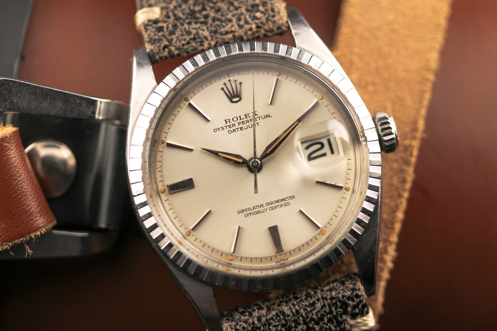 A close-up of a vintage Rolex Datejust 1603 Sword Hands-1953 with a cream dial, silver markers, and black leather strap resting elegantly on a brown surface.