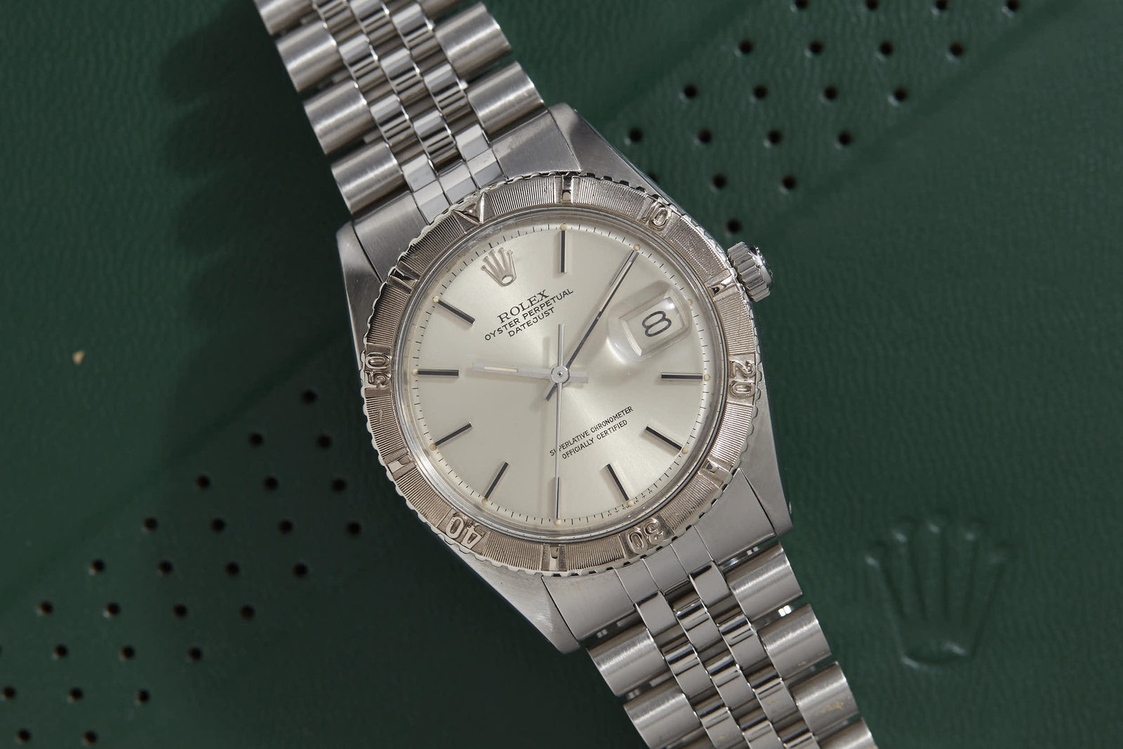 A Rolex Turn-O-Graph "Thunderbird" wristwatch from Rolex rests diagonally on a green textured surface, partially displaying the Rolex crown logo.