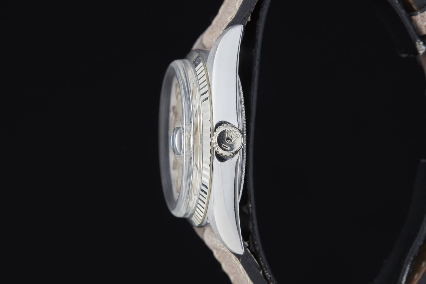 Side view of the Rolex Day Date by Rolex, featuring a silver case, black leather strap, and an engraved logo on the crown, set against a solid black background.