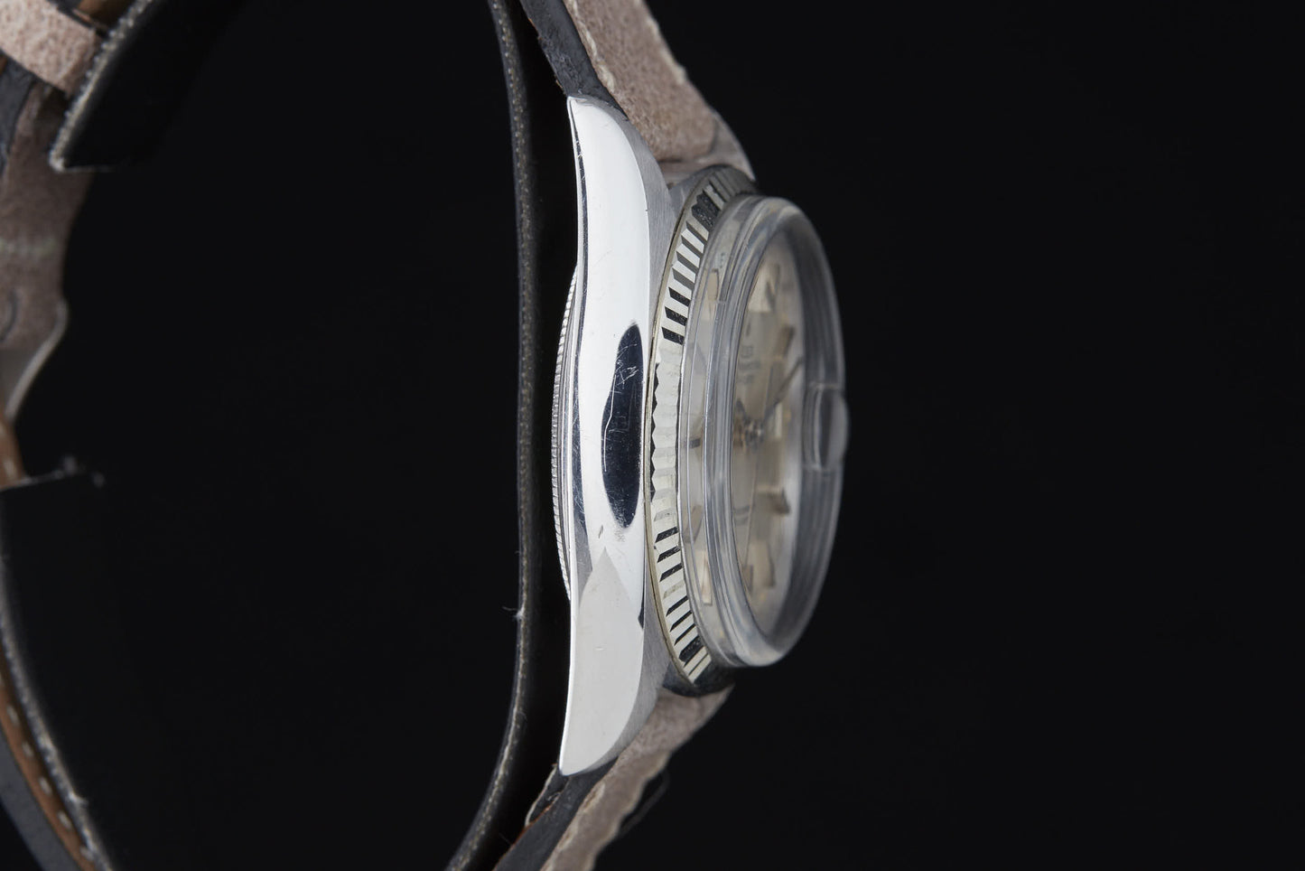 A close-up side view of the Rolex Day Date by Rolex, featuring a round silver case, textured bezel, light-colored dial, and leather strap, inspired by the classic Day-Date Reference 6511 with automatic movement against a black background.