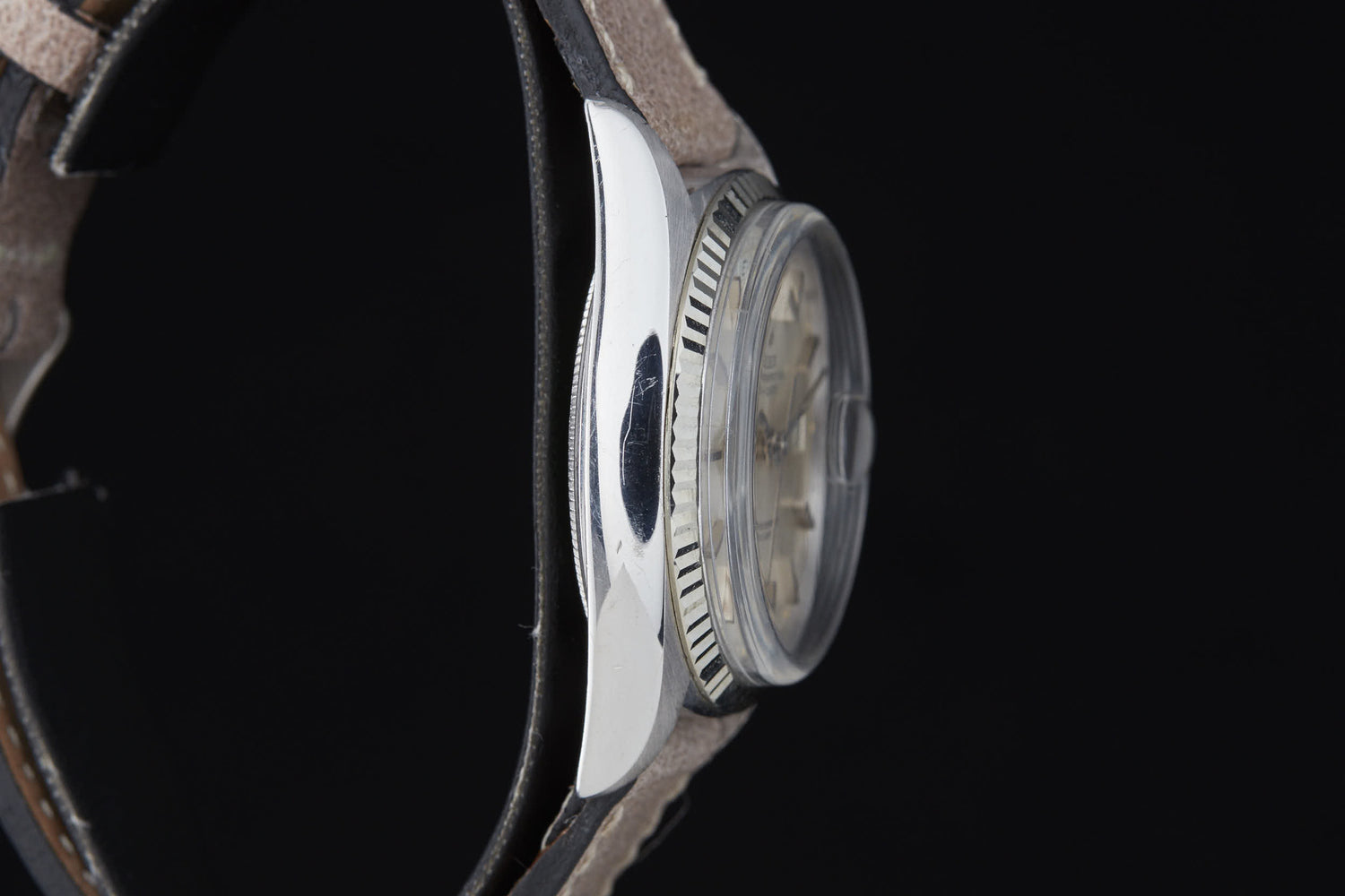 A close-up side view of the Rolex Day Date by Rolex, featuring a round silver case, textured bezel, light-colored dial, and leather strap, inspired by the classic Day-Date Reference 6511 with automatic movement against a black background.