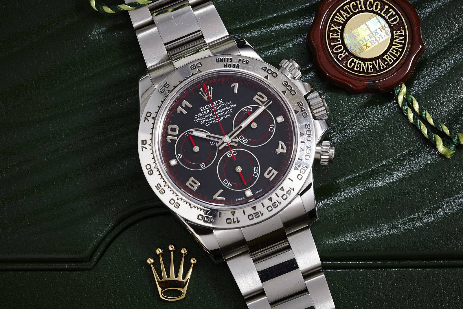 The Rolex Daytona Steel with Arabic Racing Dial, presented on a green box, is shown with original box, papers, a gold Rolex crown pin, and a brown-gold Rolex seal—highlighting this iconic steel chronograph from Rolex.