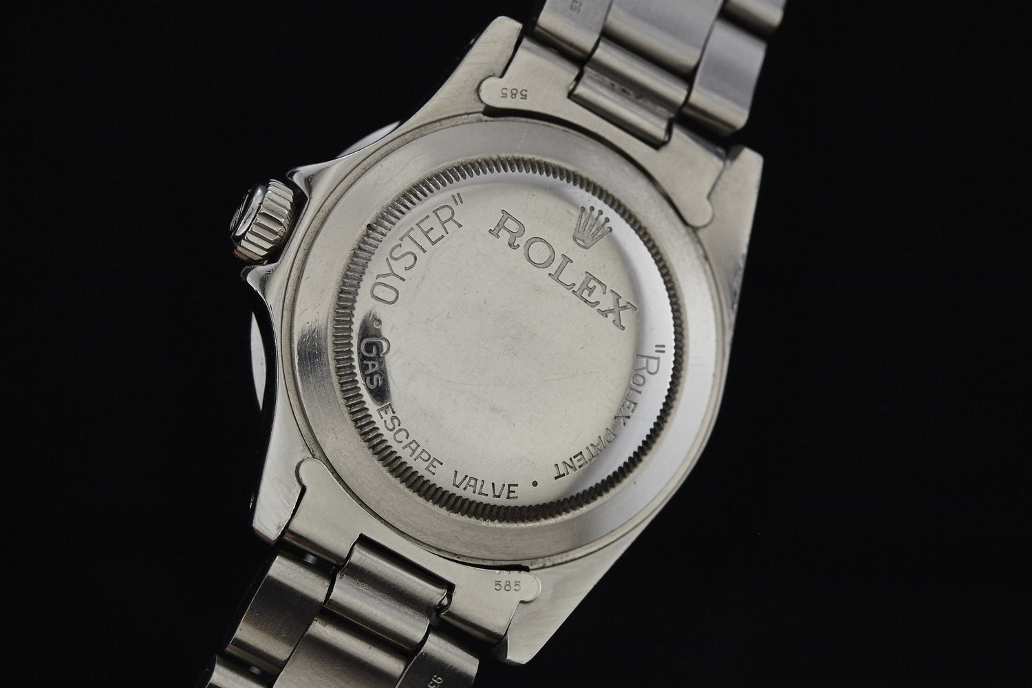 Close-up of the back of a vintage Rolex Submariner by Rolex, featuring engraved text, the Rolex crown logo, edge markings, and a partially visible metal bracelet.