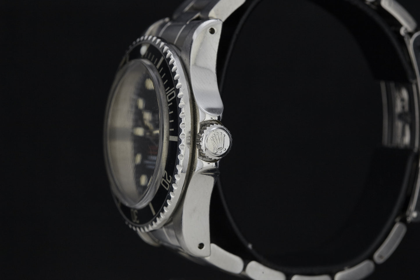 Close-up side view of a vintage Rolex Submariner by Rolex, showcasing its ridged black bezel and crown with the Rolex logo, set against a black background.
