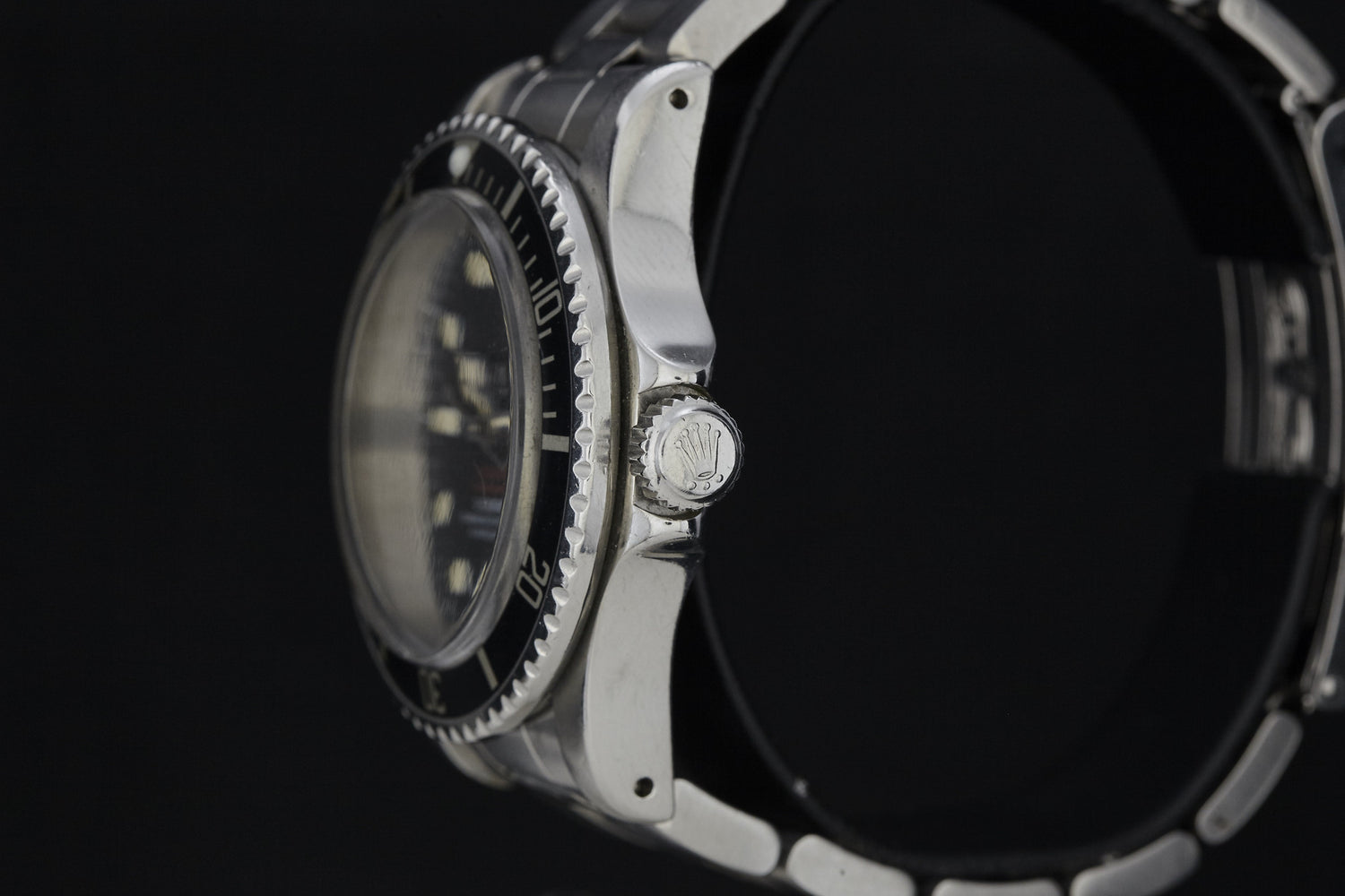 Close-up side view of a vintage Rolex Submariner by Rolex, showcasing its ridged black bezel and crown with the Rolex logo, set against a black background.