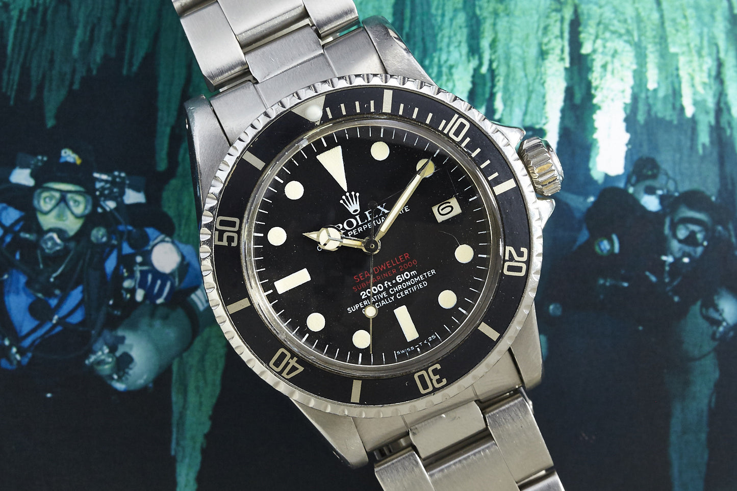 A Rolex Submariner watch with a black dial and silver bracelet is displayed prominently, set against an underwater cave diving scene with scuba divers blurred in the background.