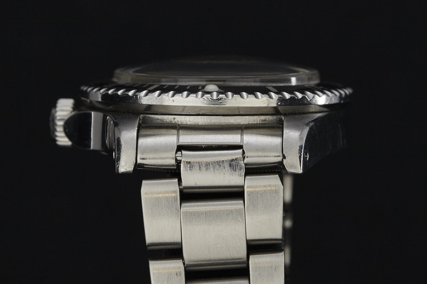 Side view of a vintage Rolex Submariner stainless steel wristwatch by Rolex, featuring a metal link band, bezel, crown, and part of the case set against a black background.