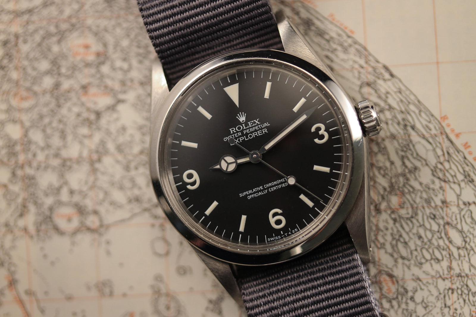 A close-up of a Rolex Explorer 1016 - 1972 by Rolex with a black dial, white markers, and nylon strap, set on a detailed map background that captures the timeless spirit of vintage adventure.