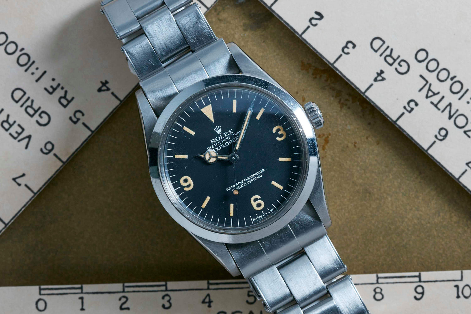 A Rolex Explorer by Rolex with a black 3-6-9 Arabic dial and silver metal band, displayed on overlapping rulers. This Everest expedition watch features bold numerals at 3, 6, and 9 o’clock.