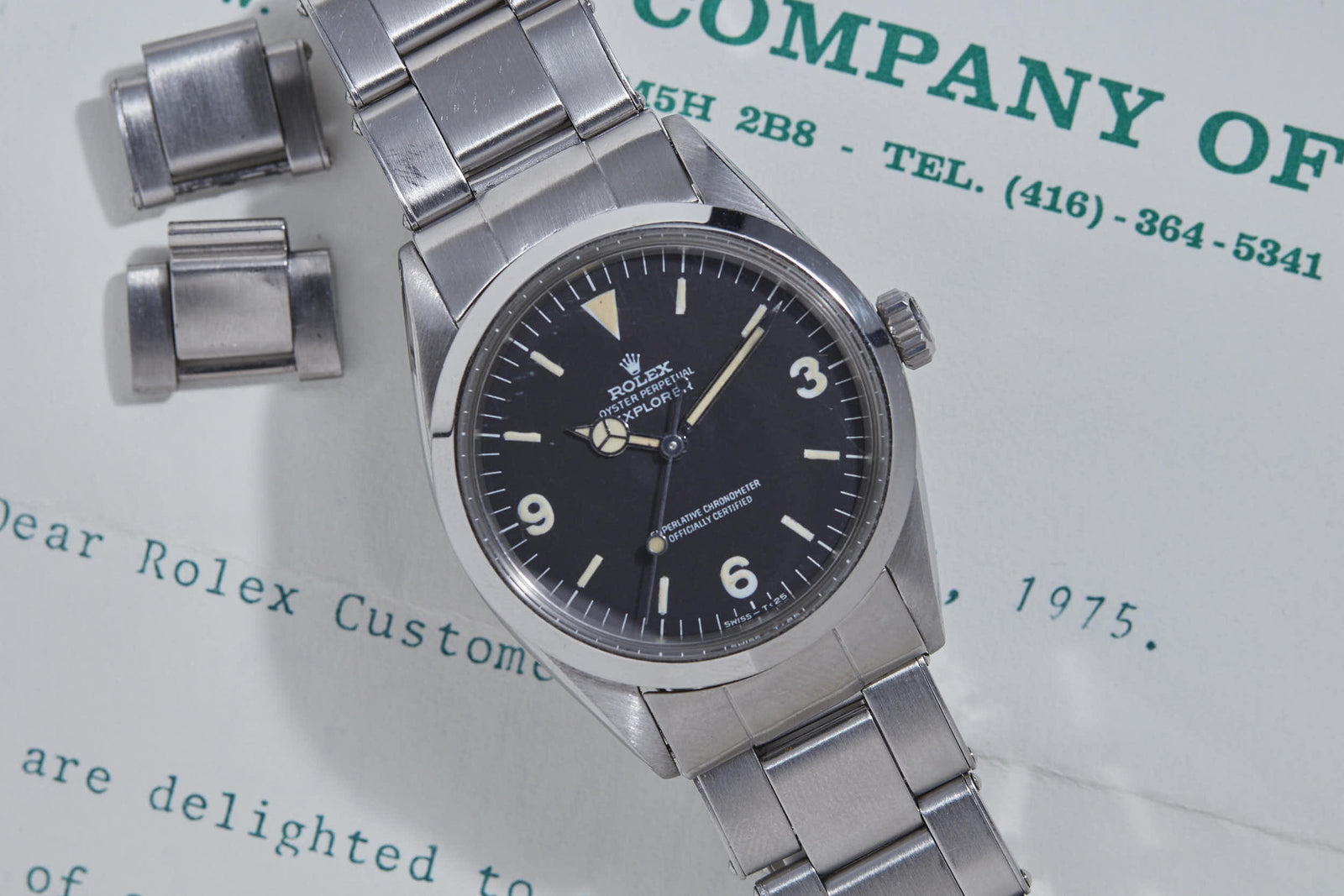 A vintage Rolex Explorer by Rolex with a stainless steel band rests on a 1975-dated letter, accompanied by two extra links beside the watch.