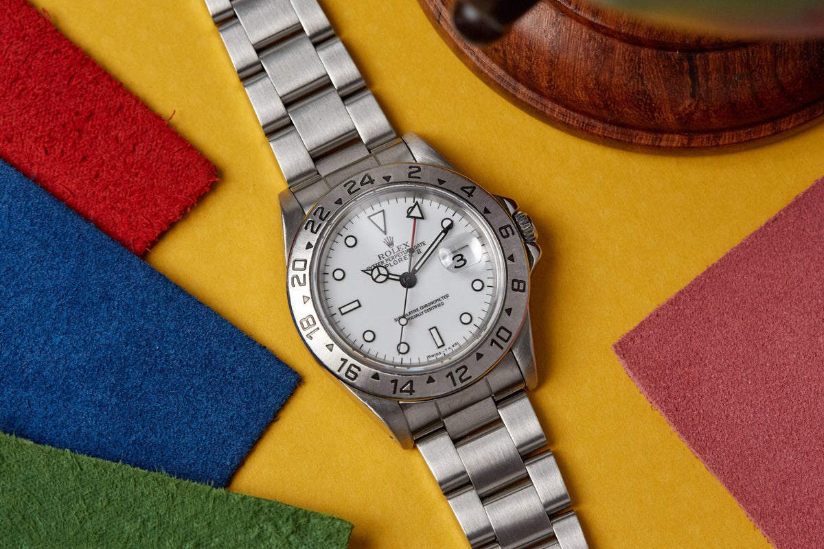 Silver stainless steel watch with white dial, numbered bezel, and matching bracelet on colorful background.