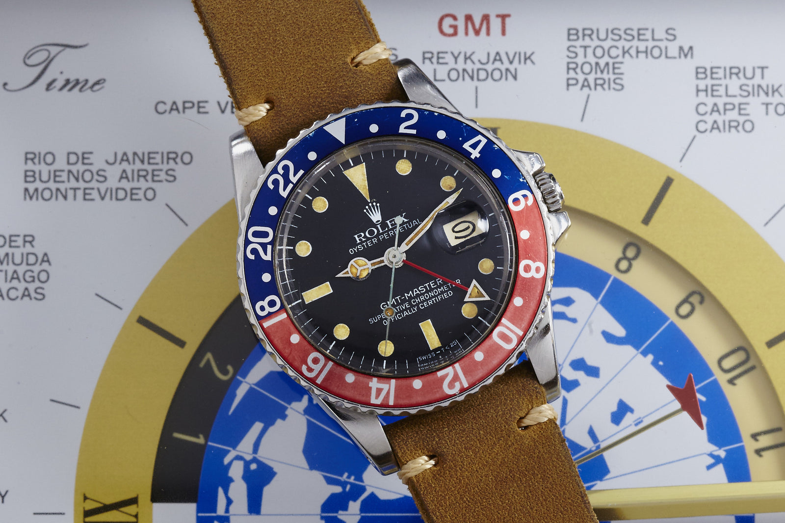 A Rolex GMT-Master wristwatch by Rolex, featuring a Pepsi bezel and brown leather strap, is displayed on a world time map with city names and a compass graphic in the background.