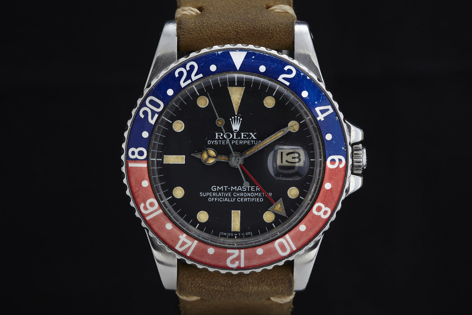 A close-up of the Rolex GMT-Master by Rolex, featuring a classic Pepsi bezel, black dial, beige hour markers, a brown leather strap, and a date window at 3 o’clock.