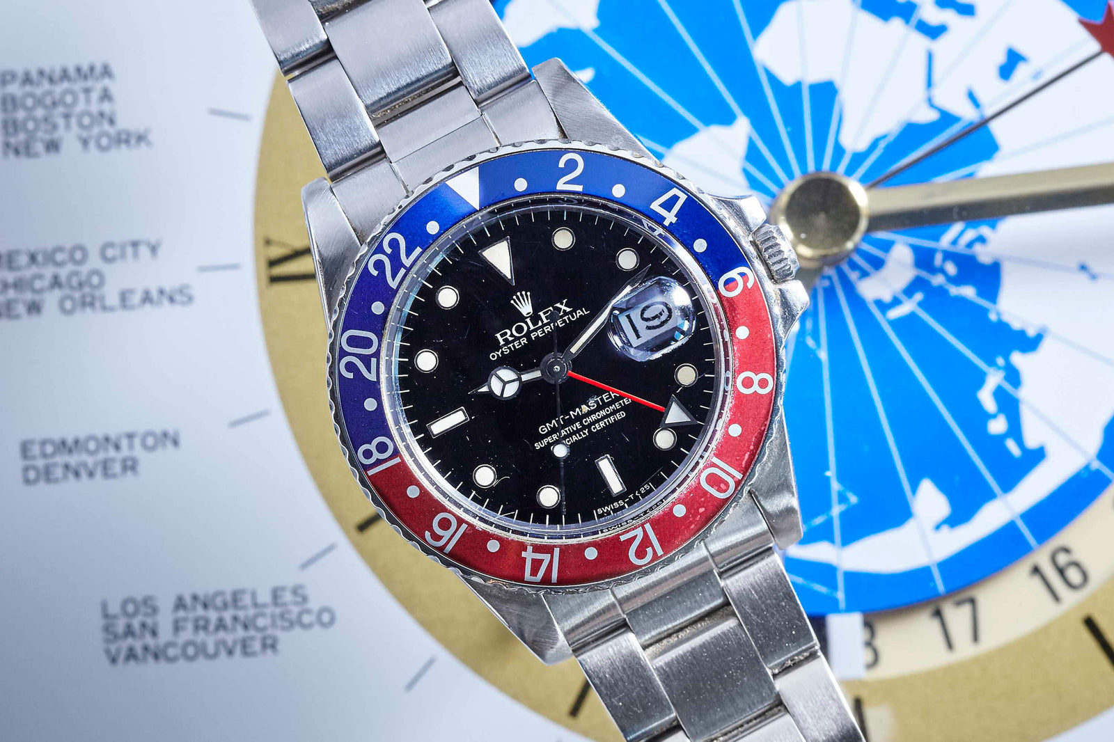 A close-up of the Rolex GMT Master 16750 by Rolex with a red and blue bezel rests on a world time zone map, highlighting global cities. Detailed description coming soon!.