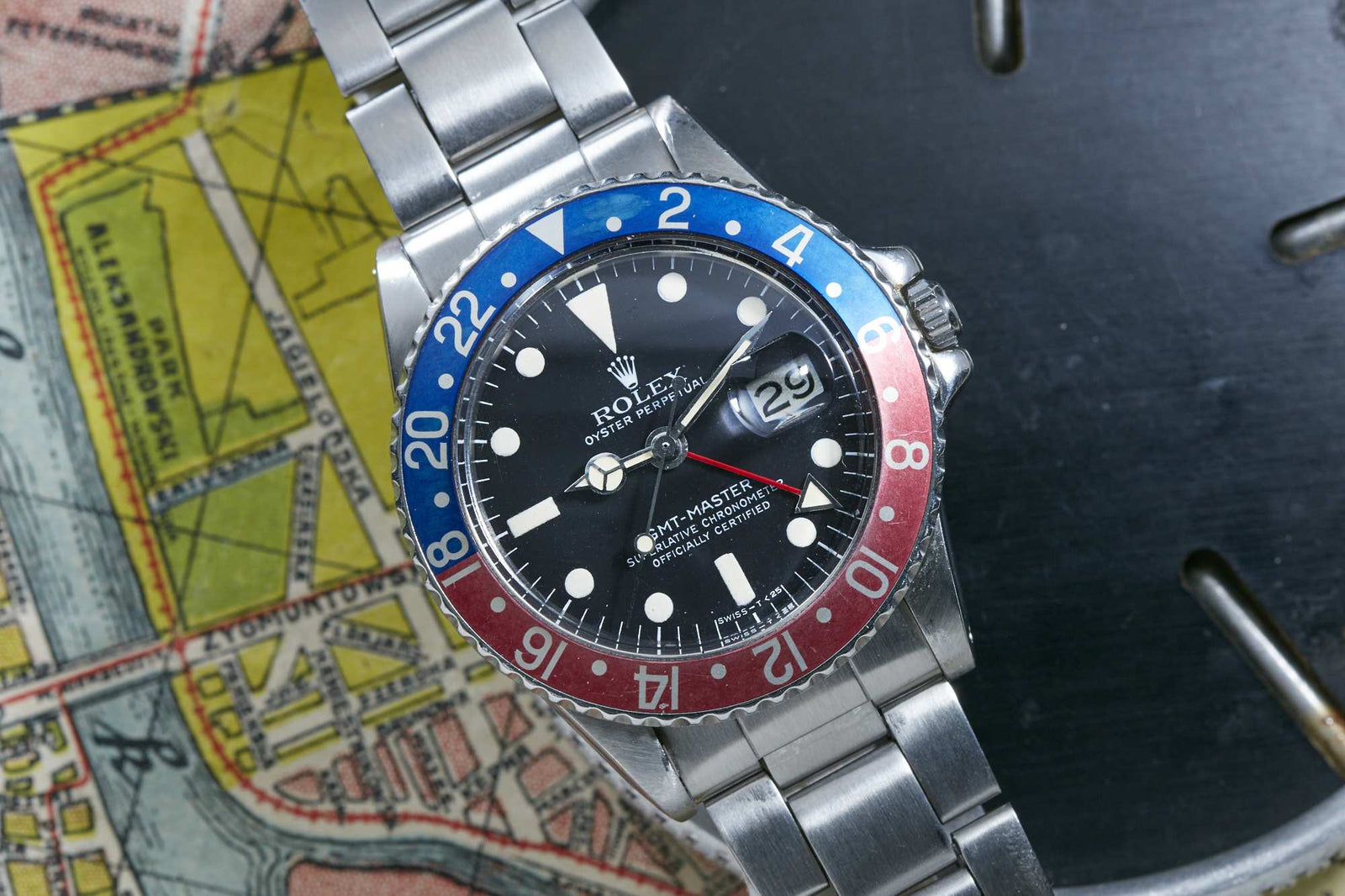 A close-up of a Rolex GMT Master by Rolex, featuring a red and blue bezel, black dial, stainless steel band, and a date window at 3 o’clock, placed on a colorful map.