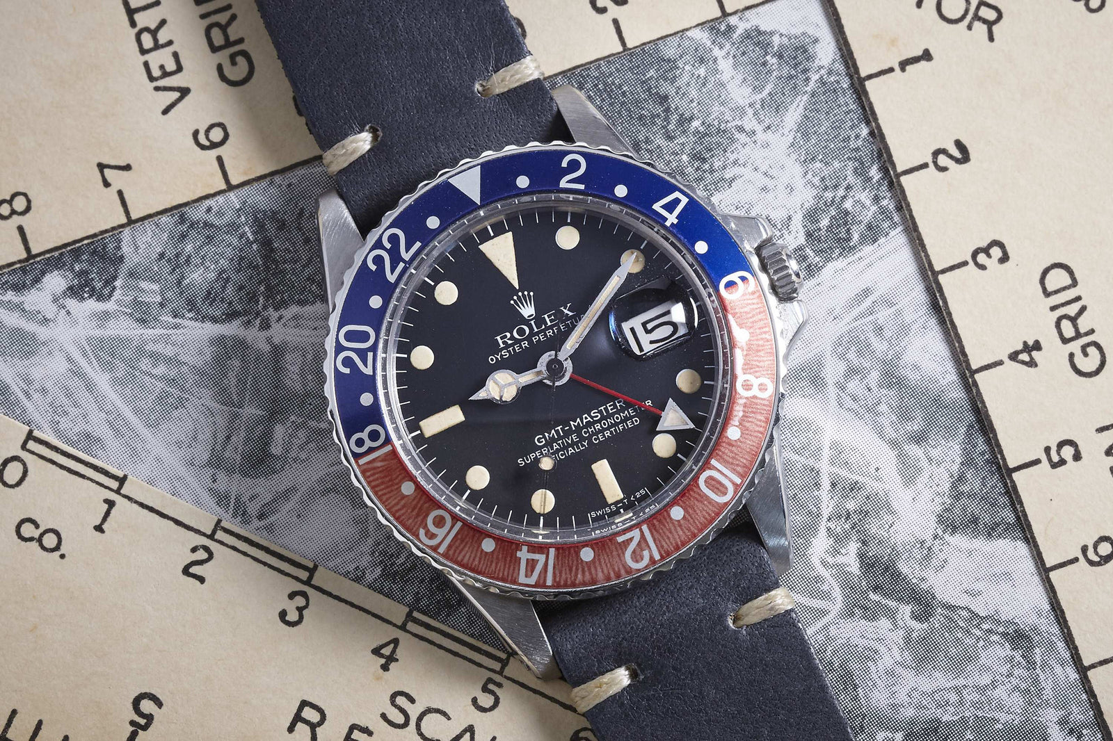 A Rolex GMT-Master by Rolex featuring a blue and red bezel, black dial, and date window, shown on a dark leather strap atop a vintage navigation chart.