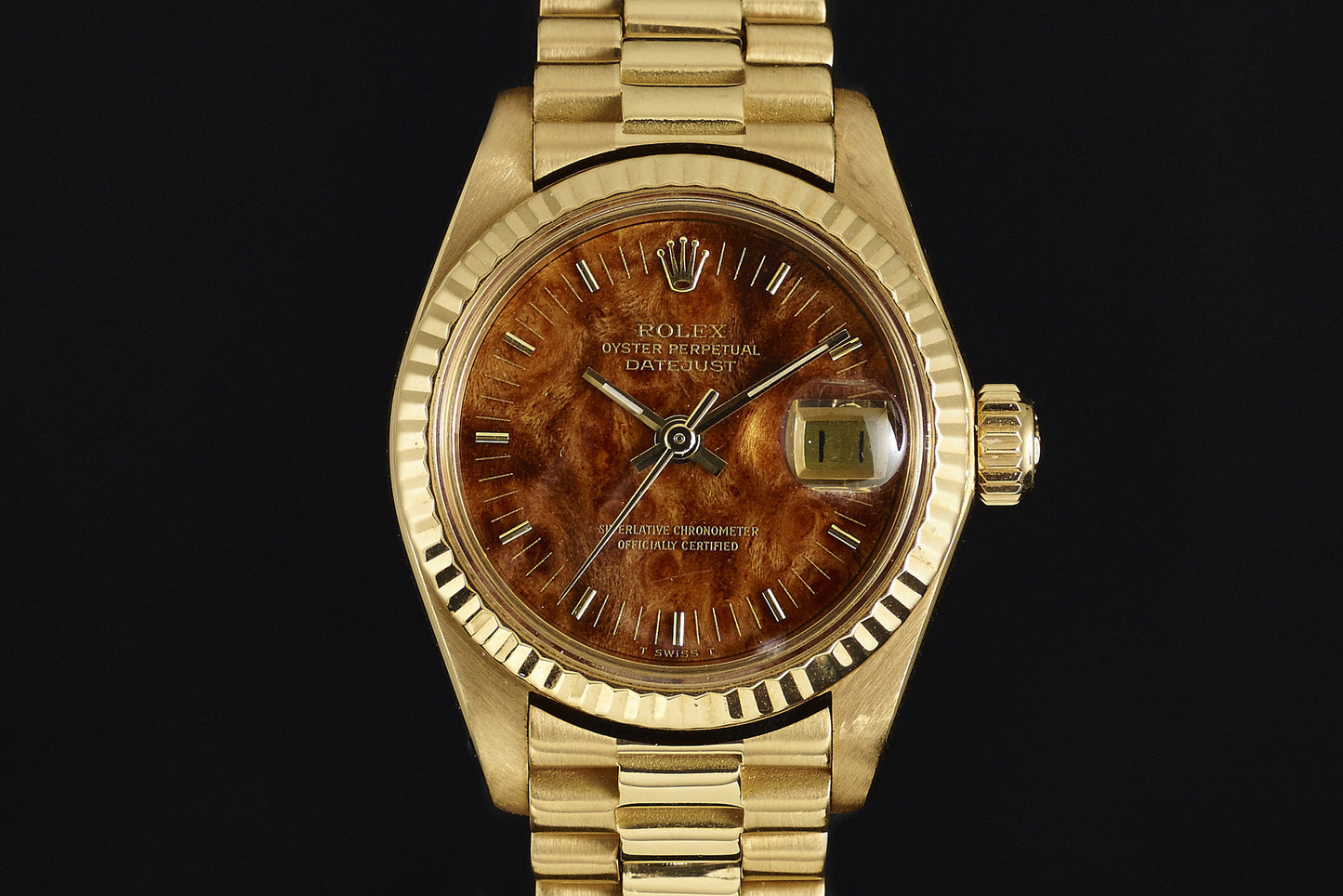 The Rolex Lady Datejust 18K Mahogany Dial is a vintage ladies' watch featuring a gold case, a unique mahogany textured dial, gold hour markers, and a date window at 3 o'clock on an elegant gold link bracelet.