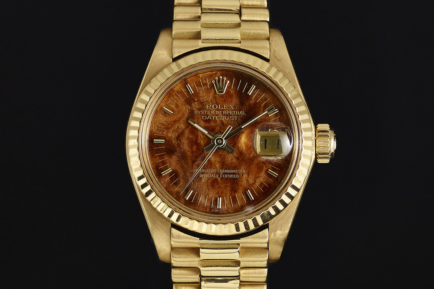 The Rolex Lady Datejust 18K Mahogany Dial is a vintage ladies' watch featuring a gold case, a unique mahogany textured dial, gold hour markers, and a date window at 3 o'clock on an elegant gold link bracelet.