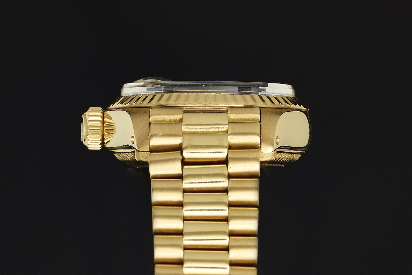 Close-up side view of the Rolex Lady Datejust 18K Mahogany Dial, featuring a fluted bezel, ridged crown, and polished gold link bracelet, set against a black background.