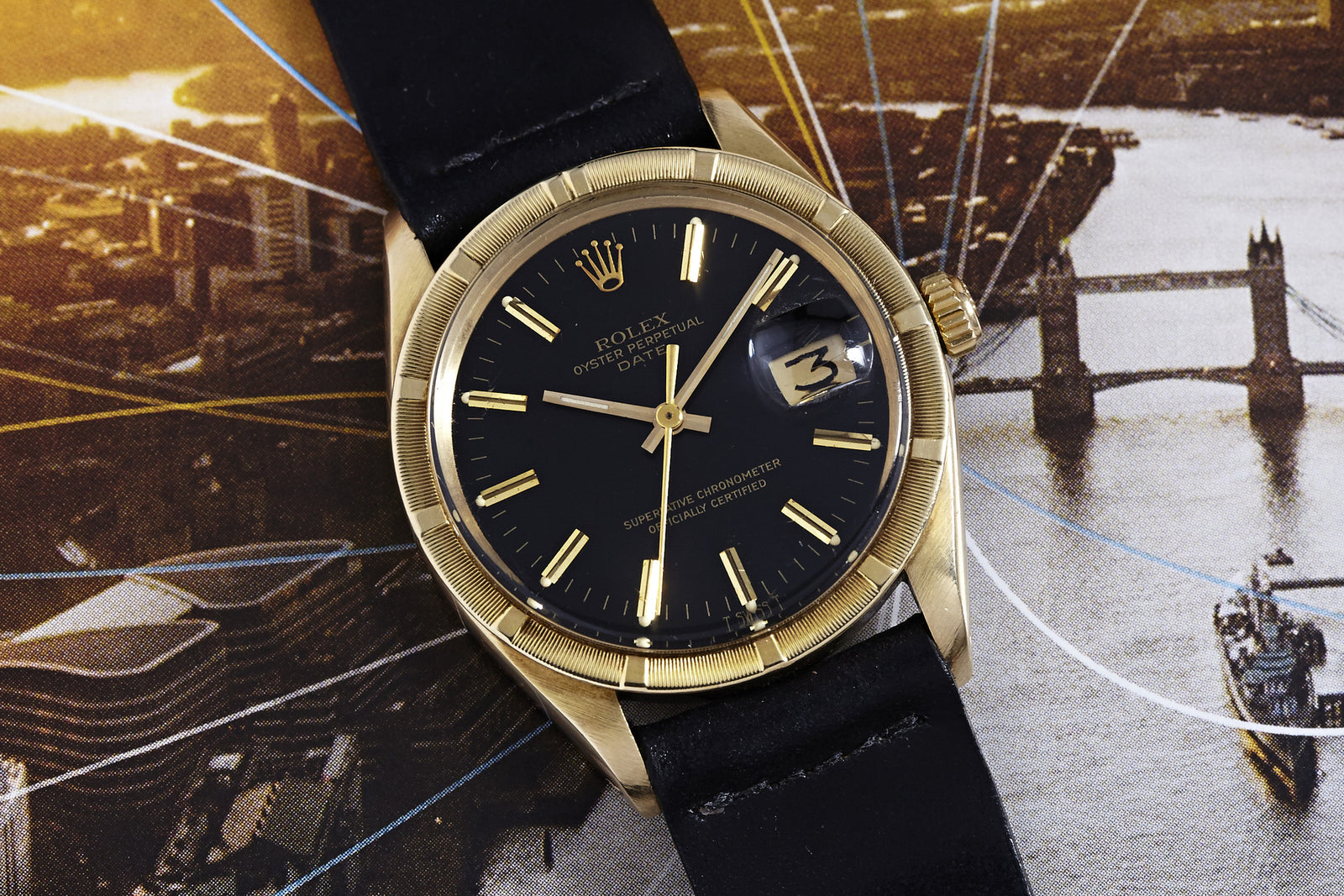 A Rolex Oyster Perpetual Date 14K with a black dial and leather strap rests on a London map, displaying the date 3 through its magnified window near the River Thames and Tower Bridge.