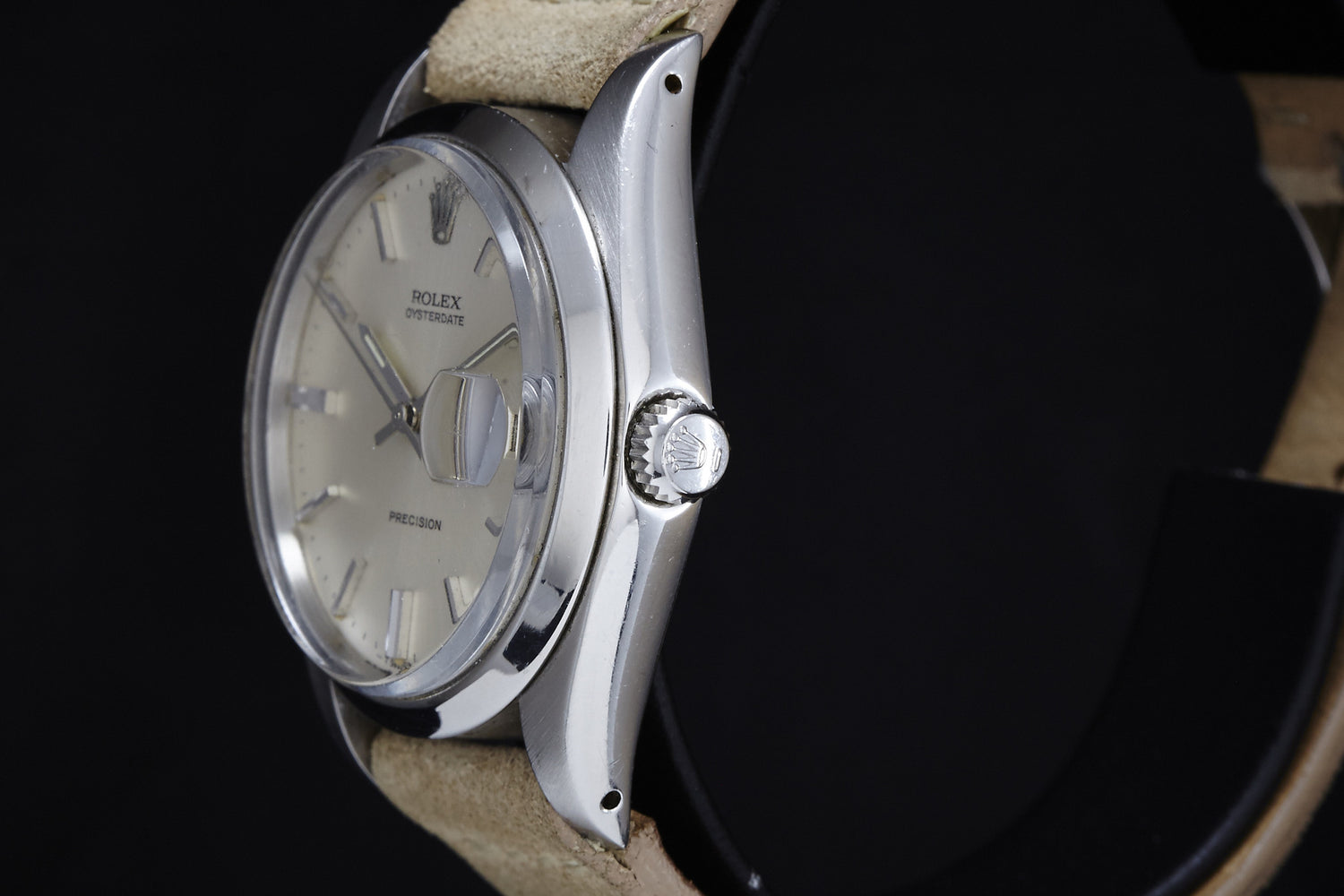 A close-up side view of the 1978 Rolex Oysterdate Precision watch by Rolex, featuring a silver case, beige leather strap, and visible crown and bezel, set against a dark background.