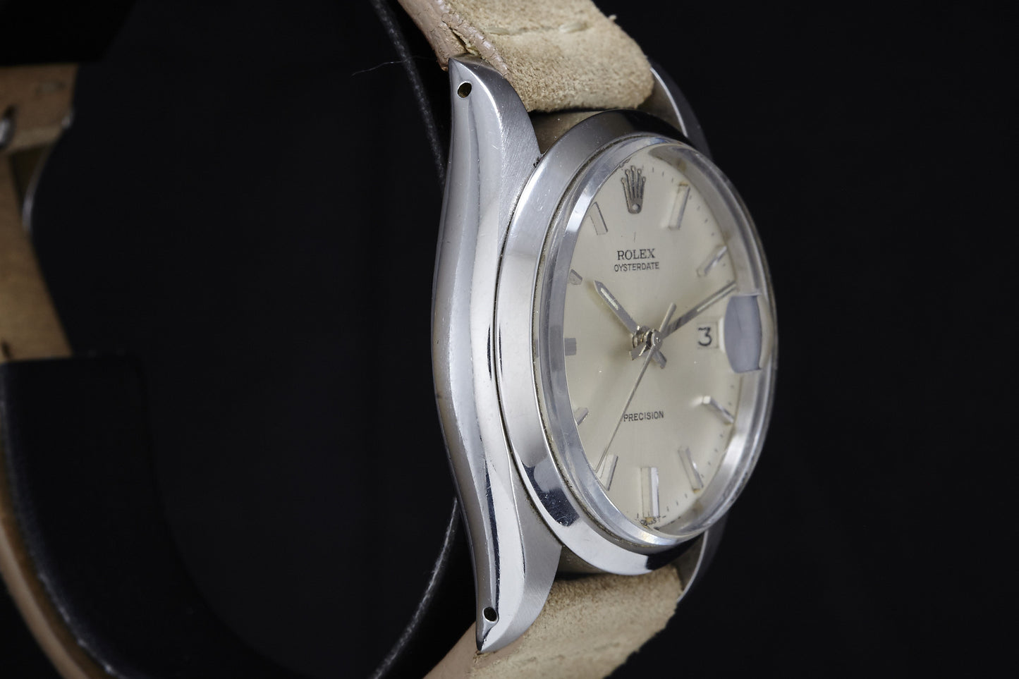 A close-up side view of the 1978 Rolex Oysterdate Precision Swiss watch with a cream dial, date window, silver hour markers, beige leather strap, and silver case, photographed against a black background.