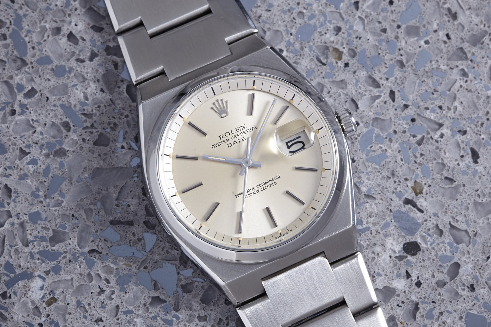 A Rolex Reference 1530 Oyster Perpetual Date with a stainless steel case and silver dial is displayed on a speckled gray stone surface.