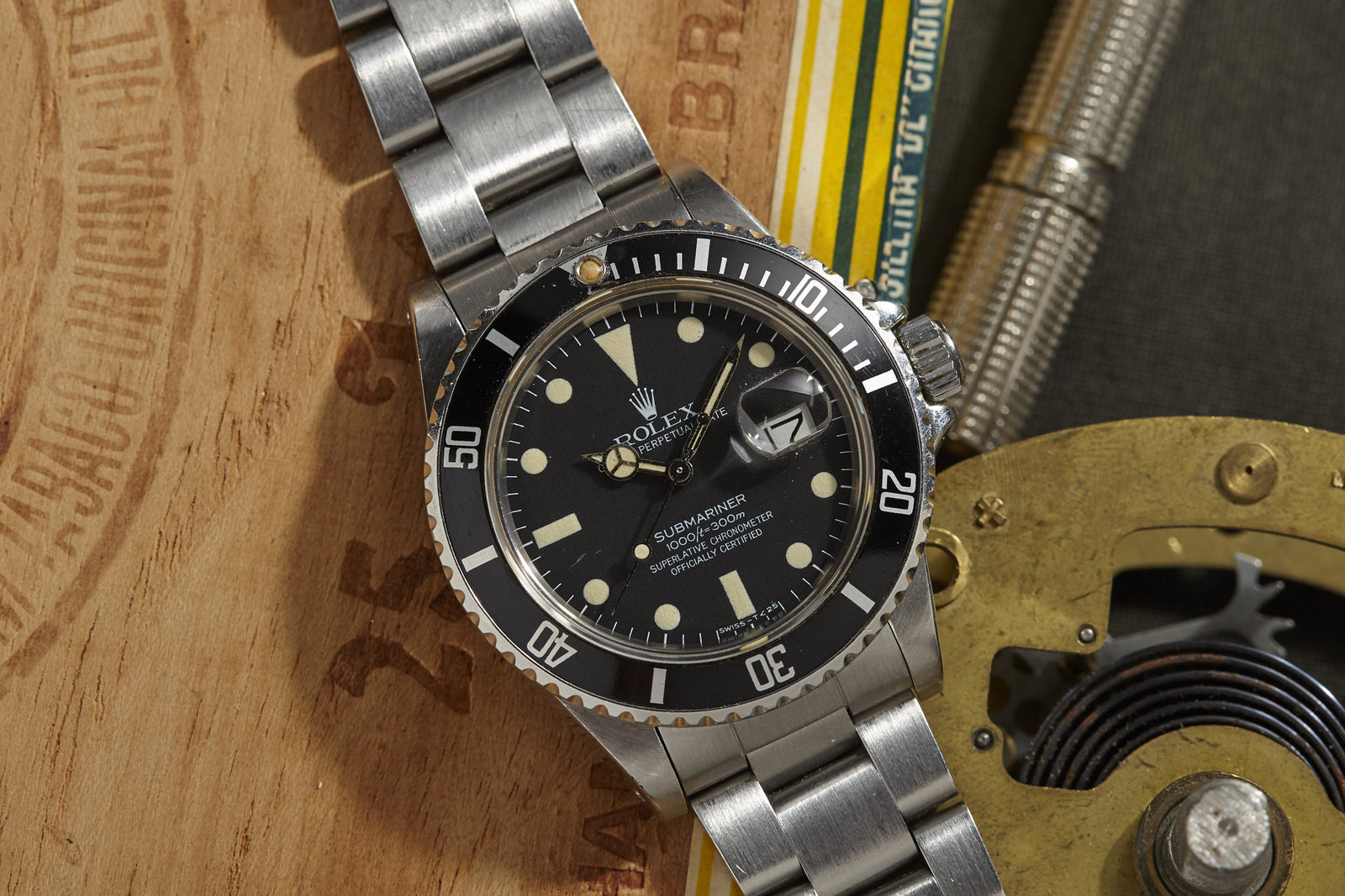 The Rolex Submariner by Rolex, featuring a classic black dial and rotating bezel with a stainless steel band, is displayed on a wooden surface among mechanical parts and a yellow-striped item.